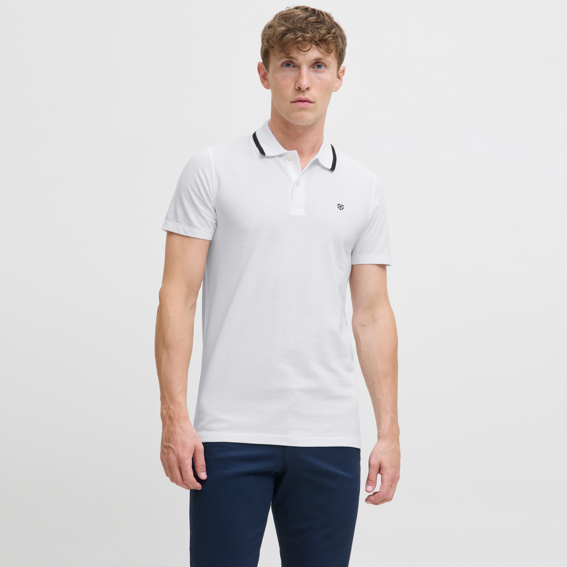 Homem com polo branca e calças azuis escuras em fundo branco