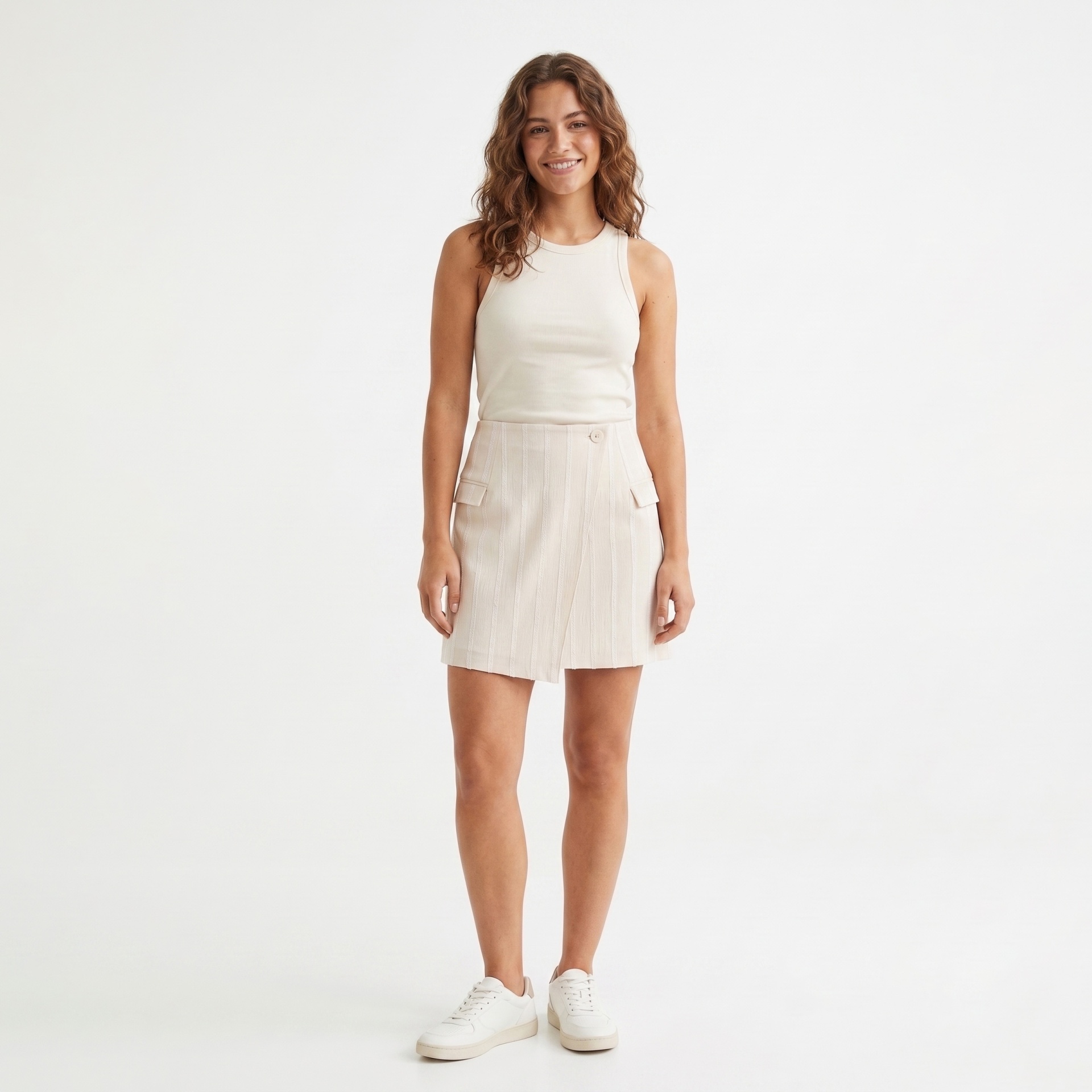 Mulher com camisola e saia bege claro e ténis brancos, em fundo branco