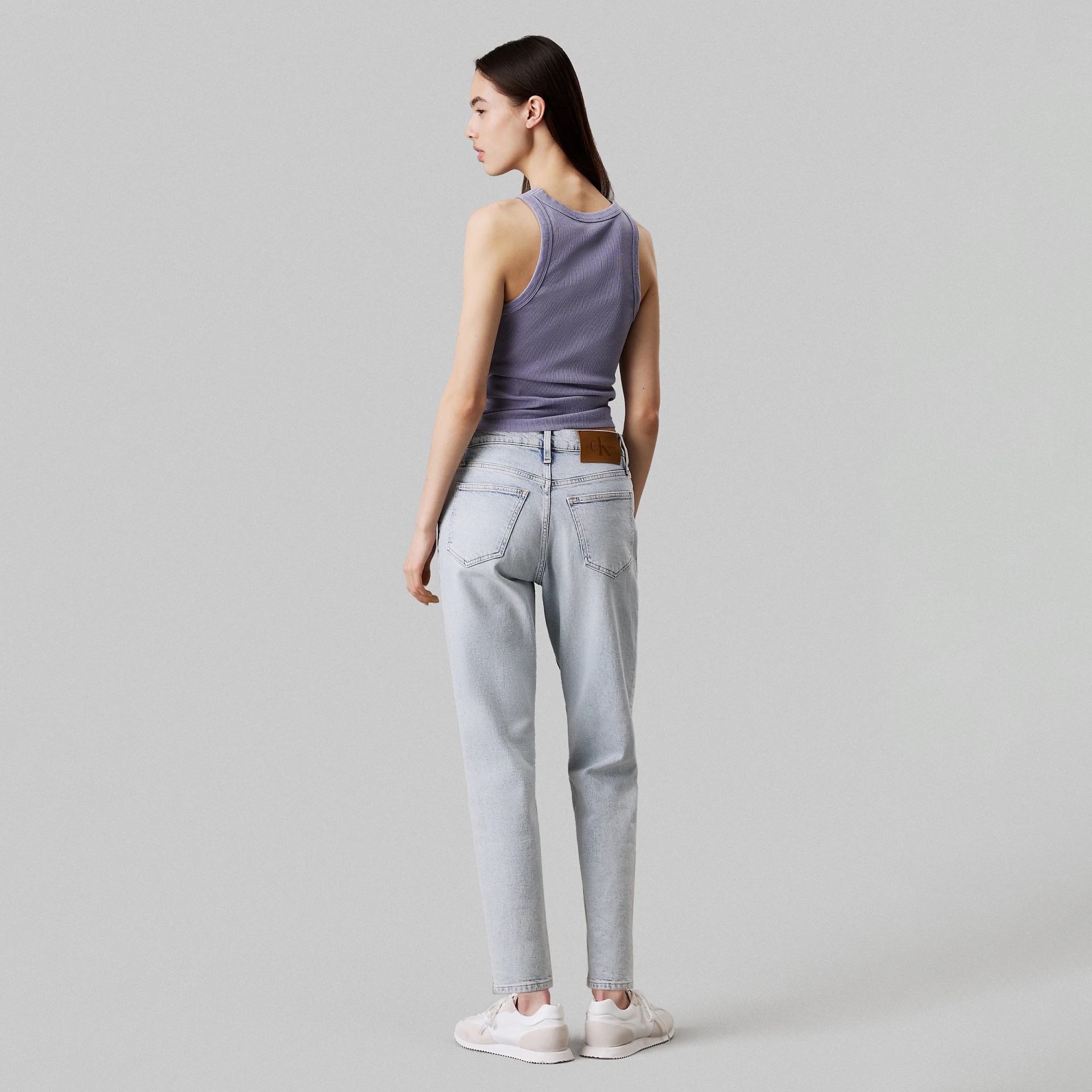 Mulher de costas com regata lilás e jeans azul claro e sapatilhas brancas