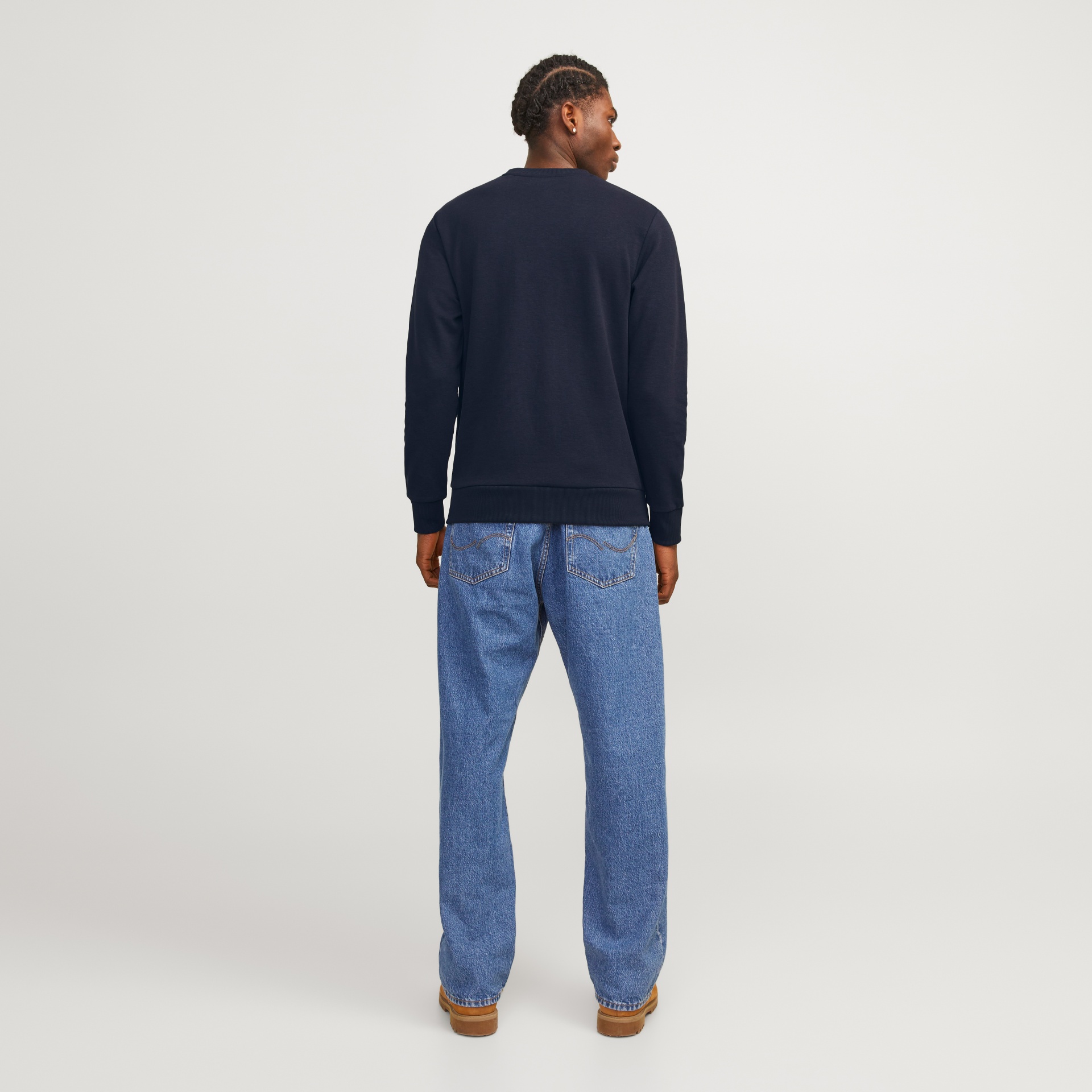 Homem de costas com sweatshirt preta, jeans azuis e botas castanhas.