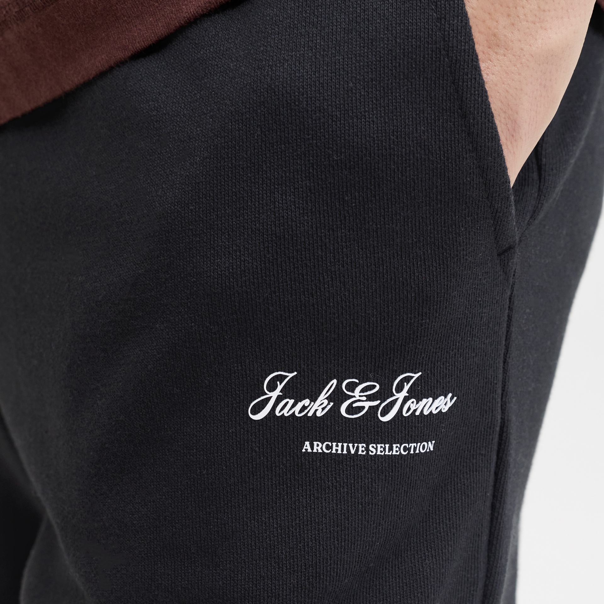 Calças pretas com texto branco Jack & Jones ARCHIVE SELECTION e mão no bolso