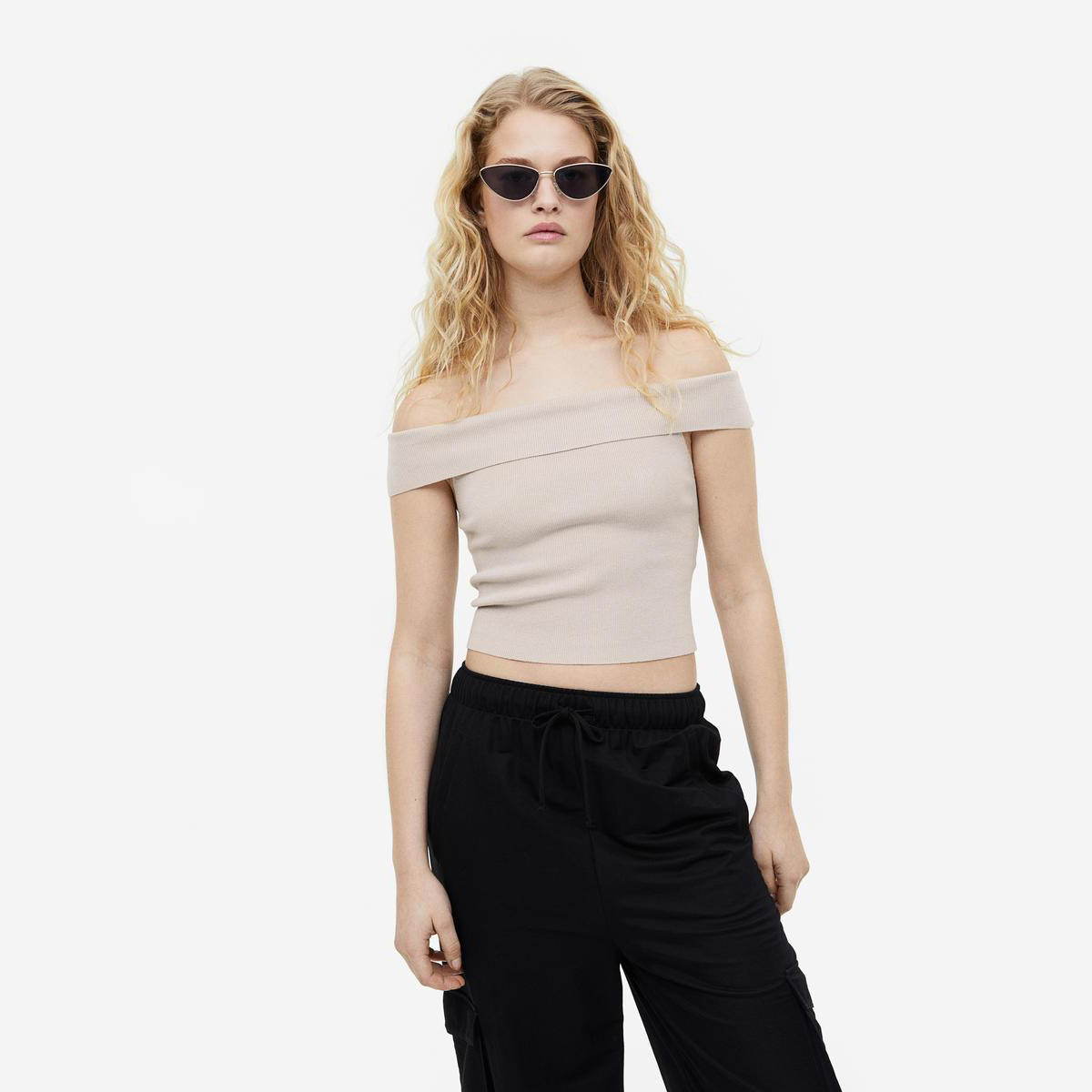 Mulher com top cropped bege canelado ombro a ombro e calças pretas com cordão na cintura
