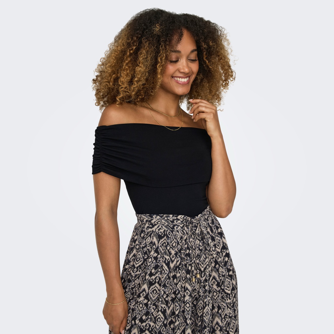 Mulher com top preto ombro a ombro e saia com padrão geométrico cinza e bege