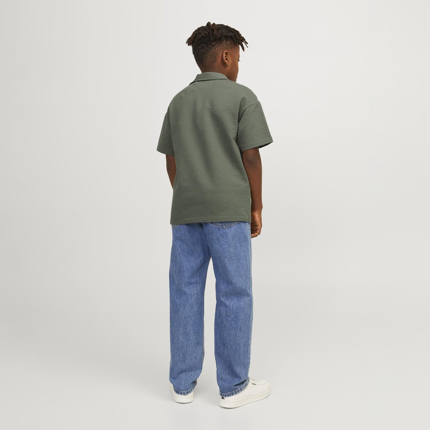 Criança de costas com camisa verde e jeans azuis