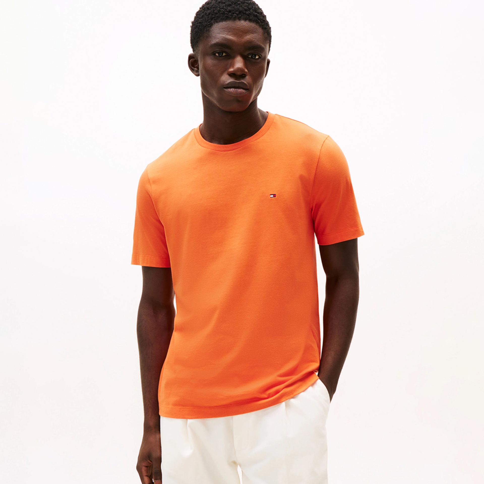 Homem a usar t-shirt laranja de manga curta com logótipo pequeno e calças brancas