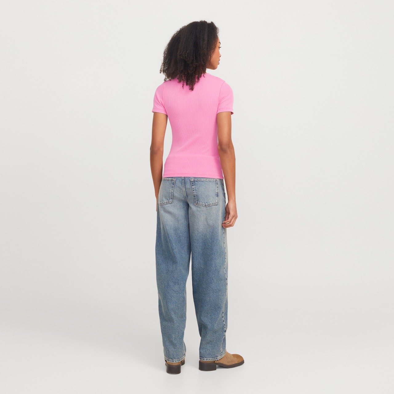 Pessoa de costas com camisola rosa e jeans largos azuis em fundo branco
