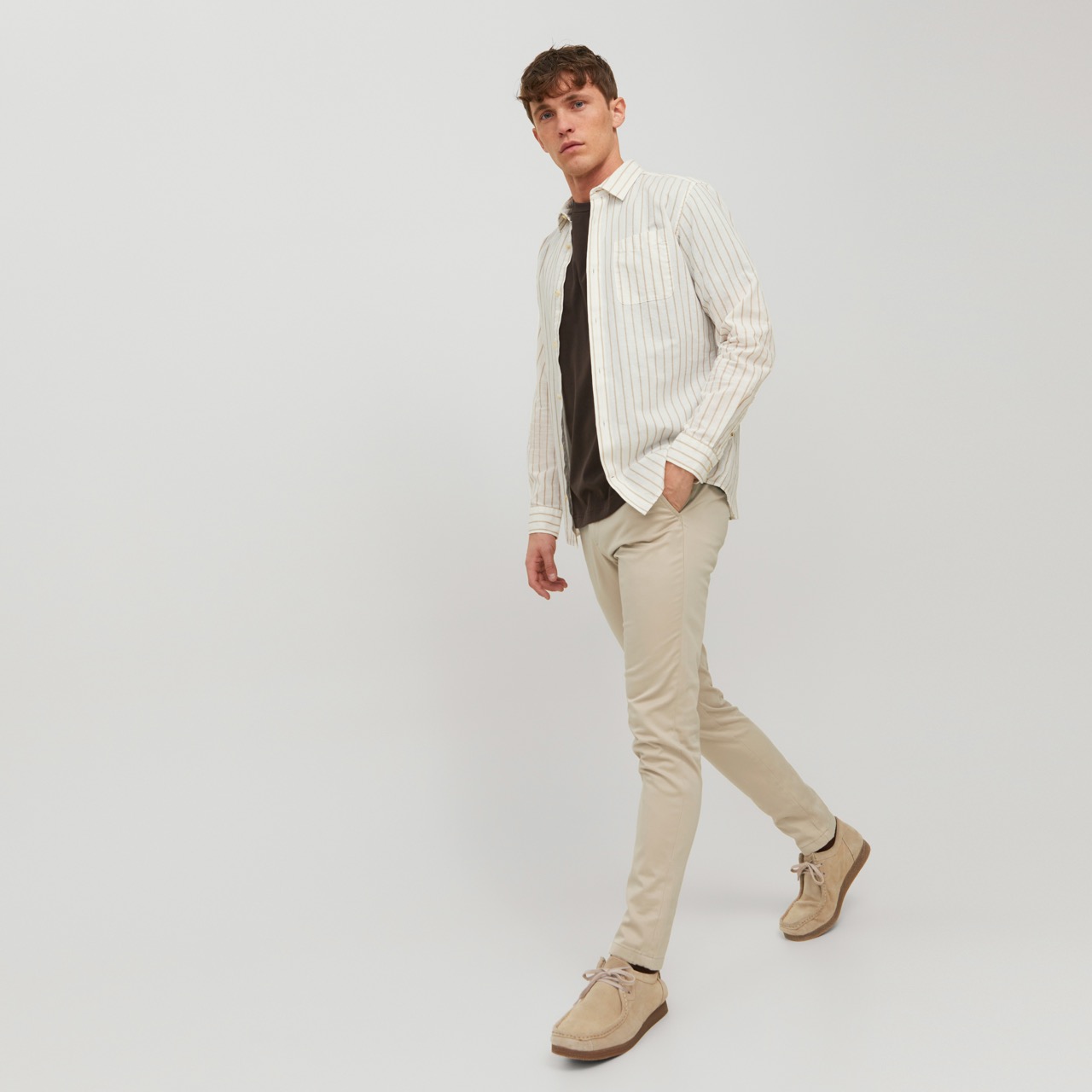 Homem com camisa branca de riscas, t-shirt preta, calças bege e sapatos castanhos claros