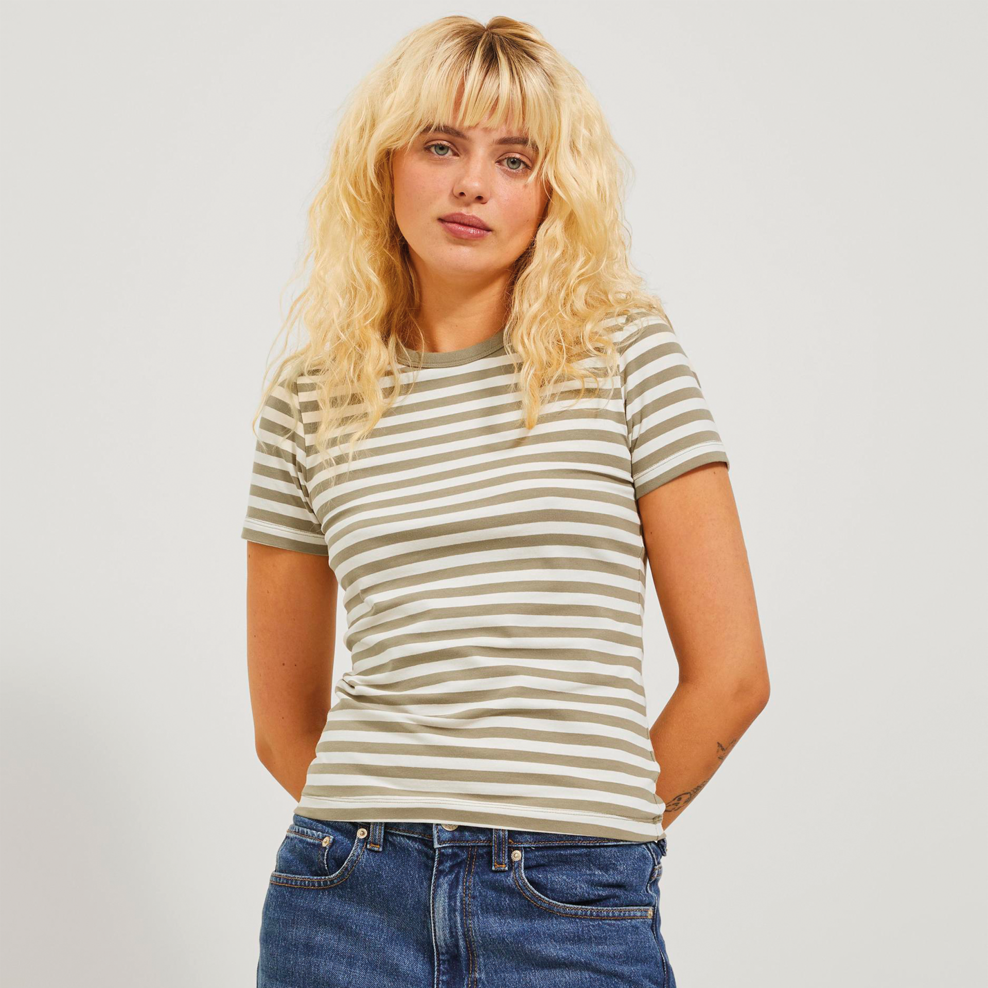 Mulher com t-shirt riscada cinzento e branco e calças jeans azuis em fundo neutro