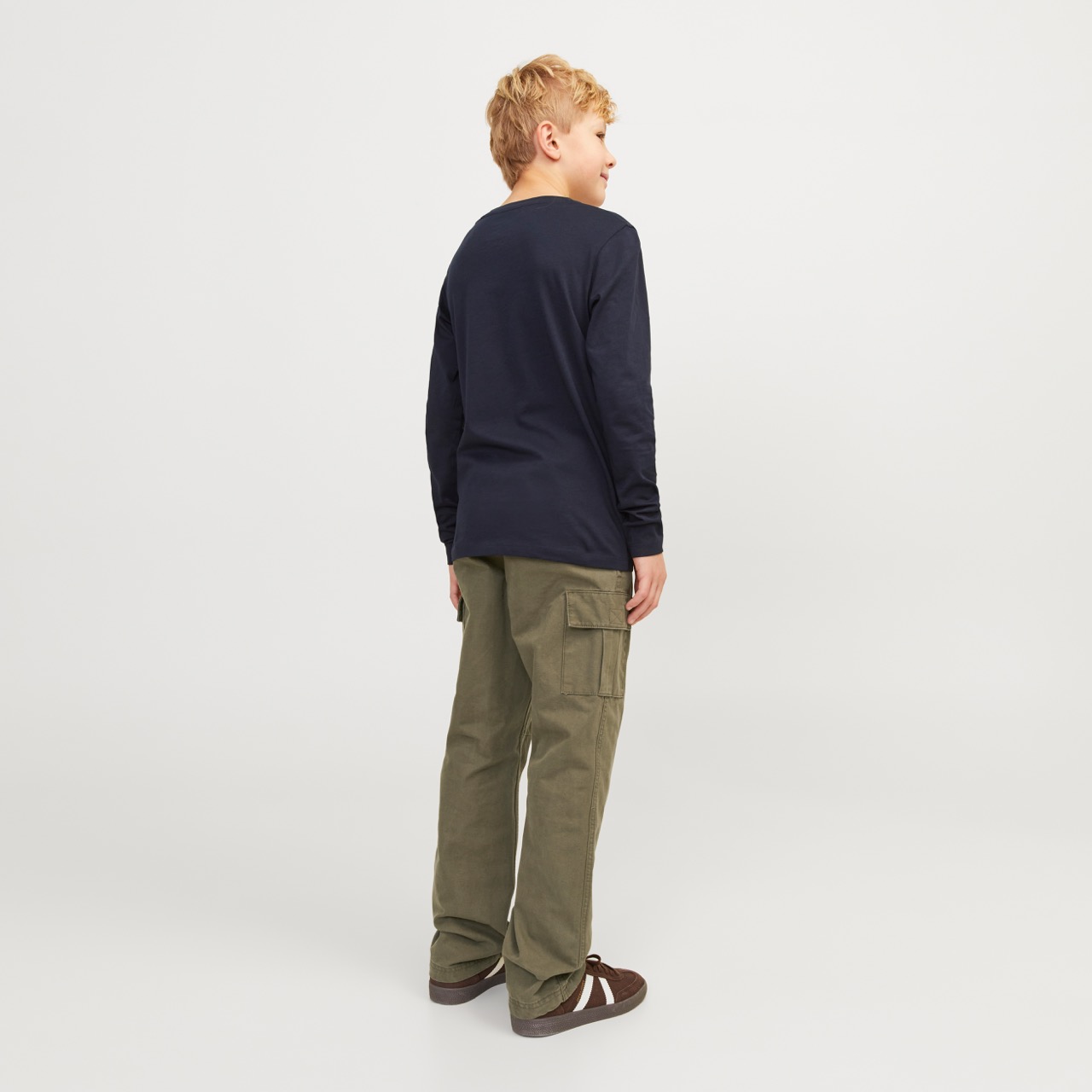 Rapaz de costas com camisola azul, calças cargo verdes e sapatos castanhos com riscas brancas