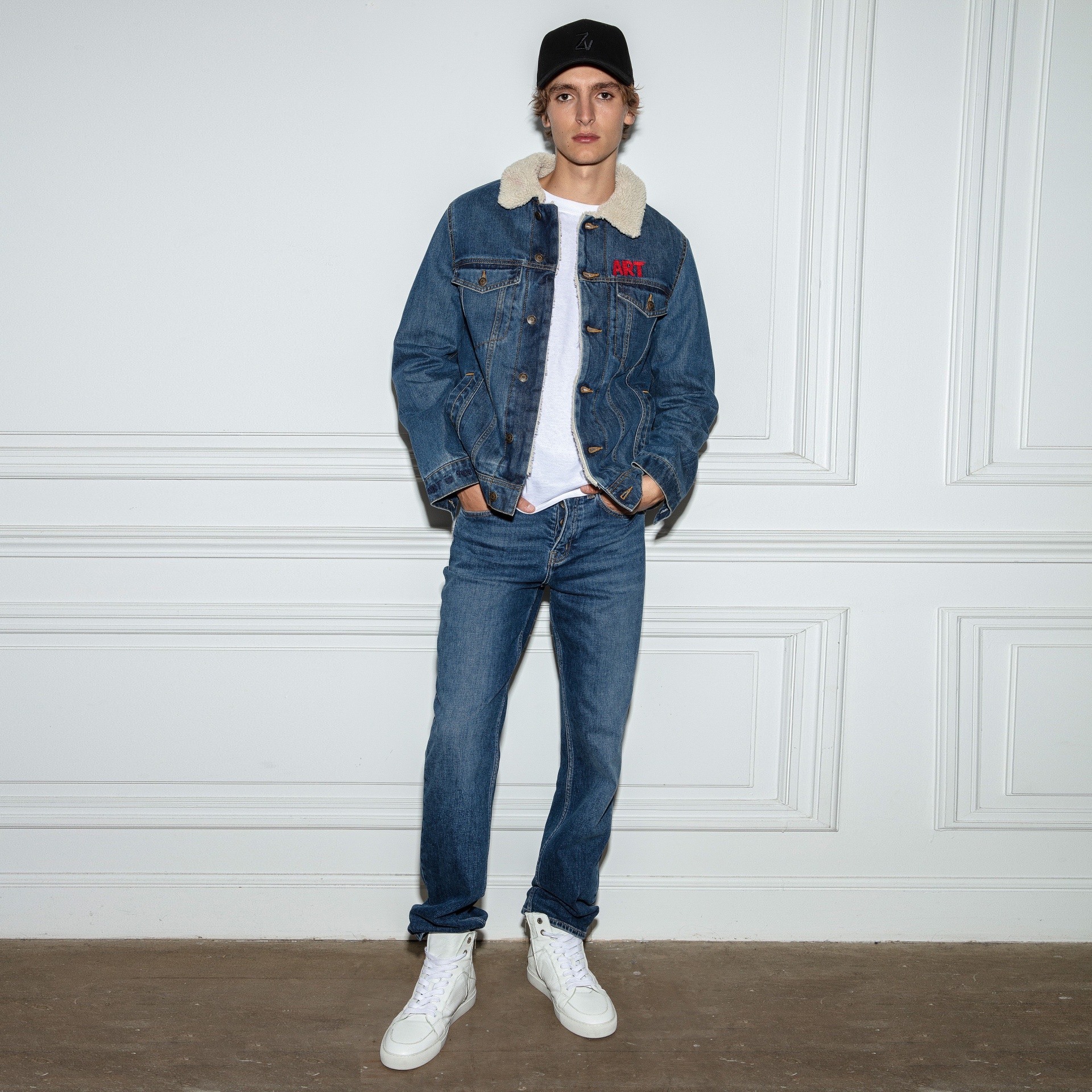 Modelo com casaco de ganga azul de gola de pelo sintético ART, jeans azuis, t-shirt branca, boné preto e sapatilhas brancas.