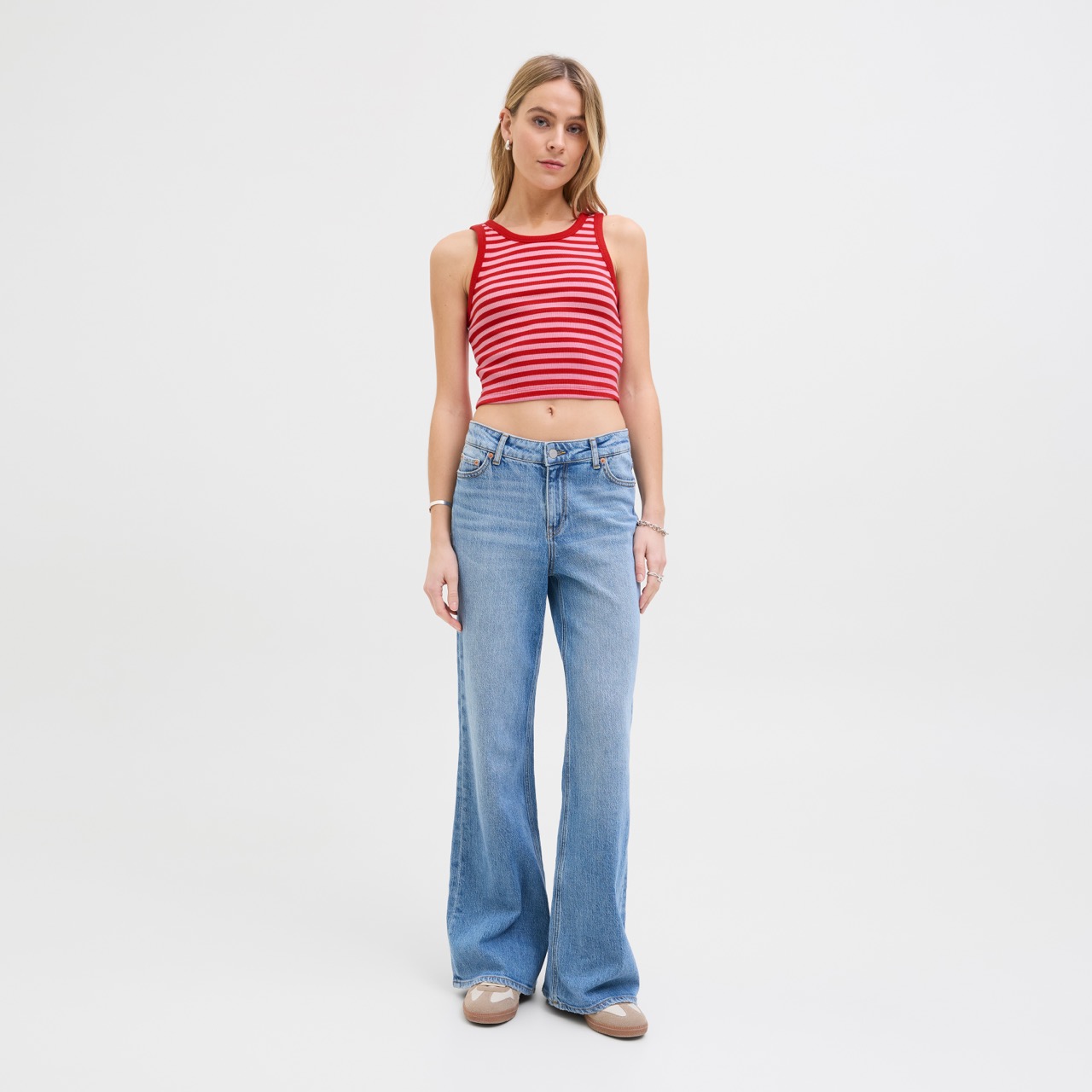 Mulher de pé com top cropped vermelho às riscas e jeans azuis largos