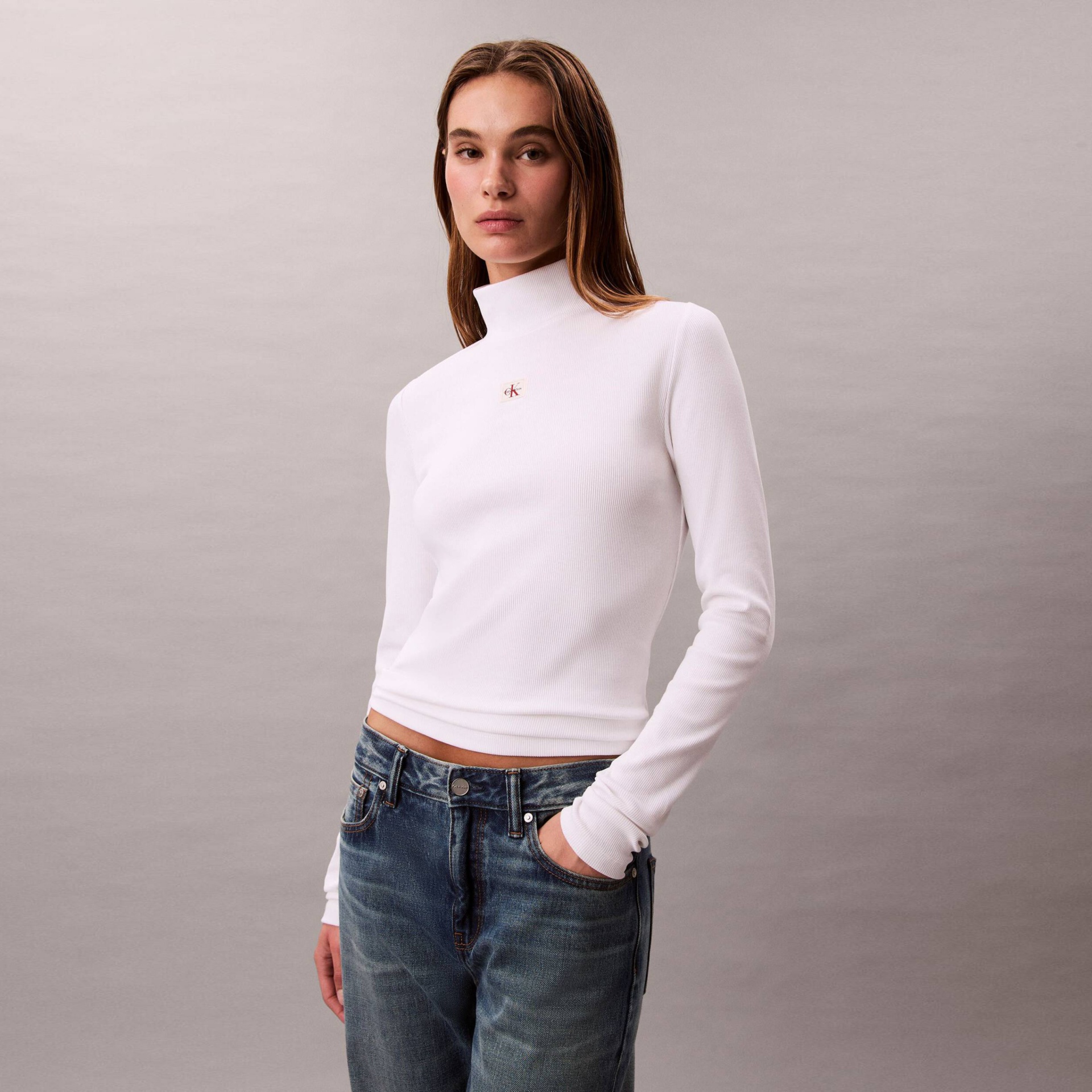 Camisola branca de gola alta com logótipo ck usada por mulher com jeans