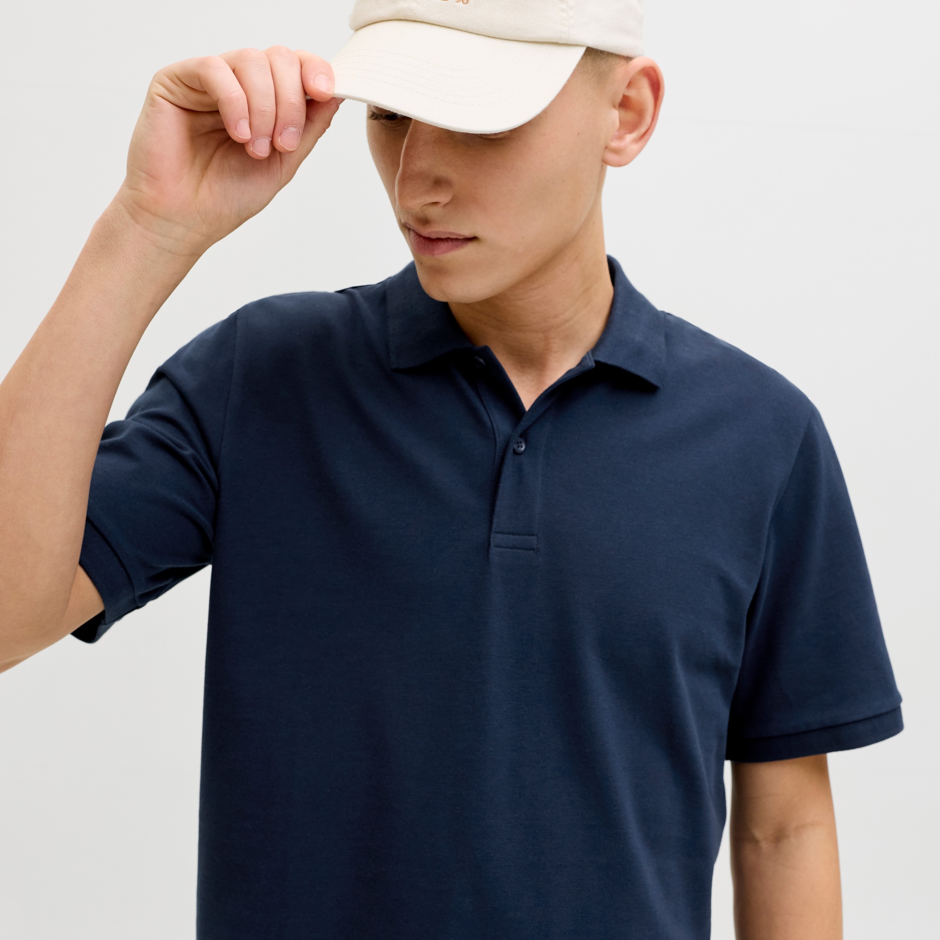 Homem a usar camisola polo azul e boné bege, segurando a aba do boné