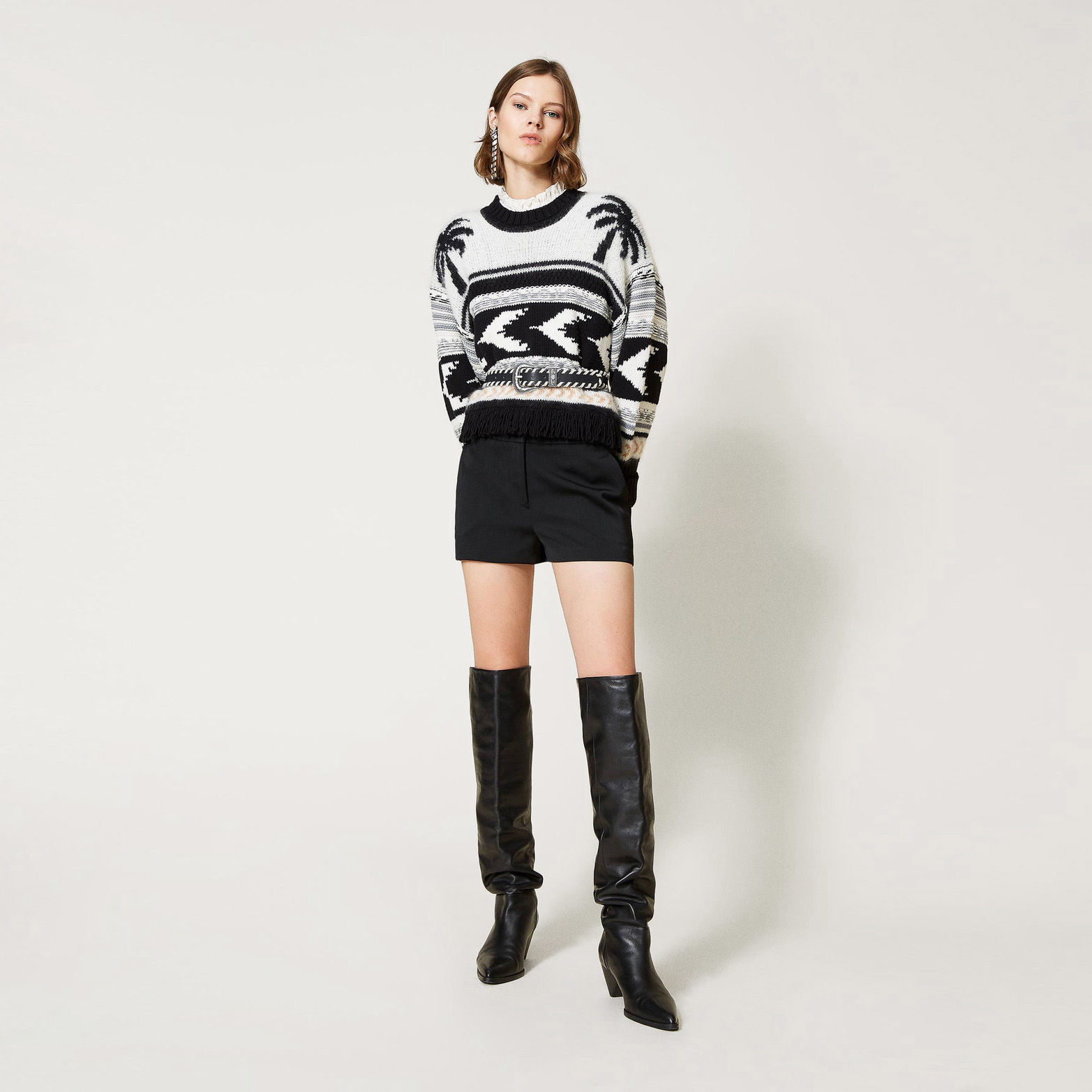 Mulher com camisola de malha preta e branca, calções pretos e botas pretas altas.