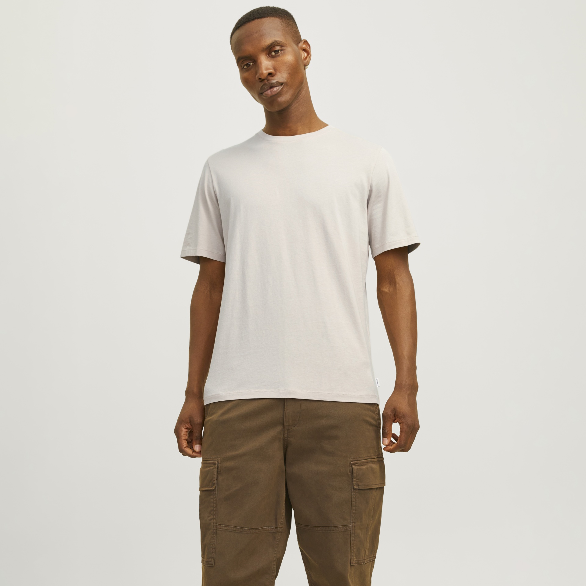 Homem com t-shirt branca e calças cargo castanhas num fundo branco simples