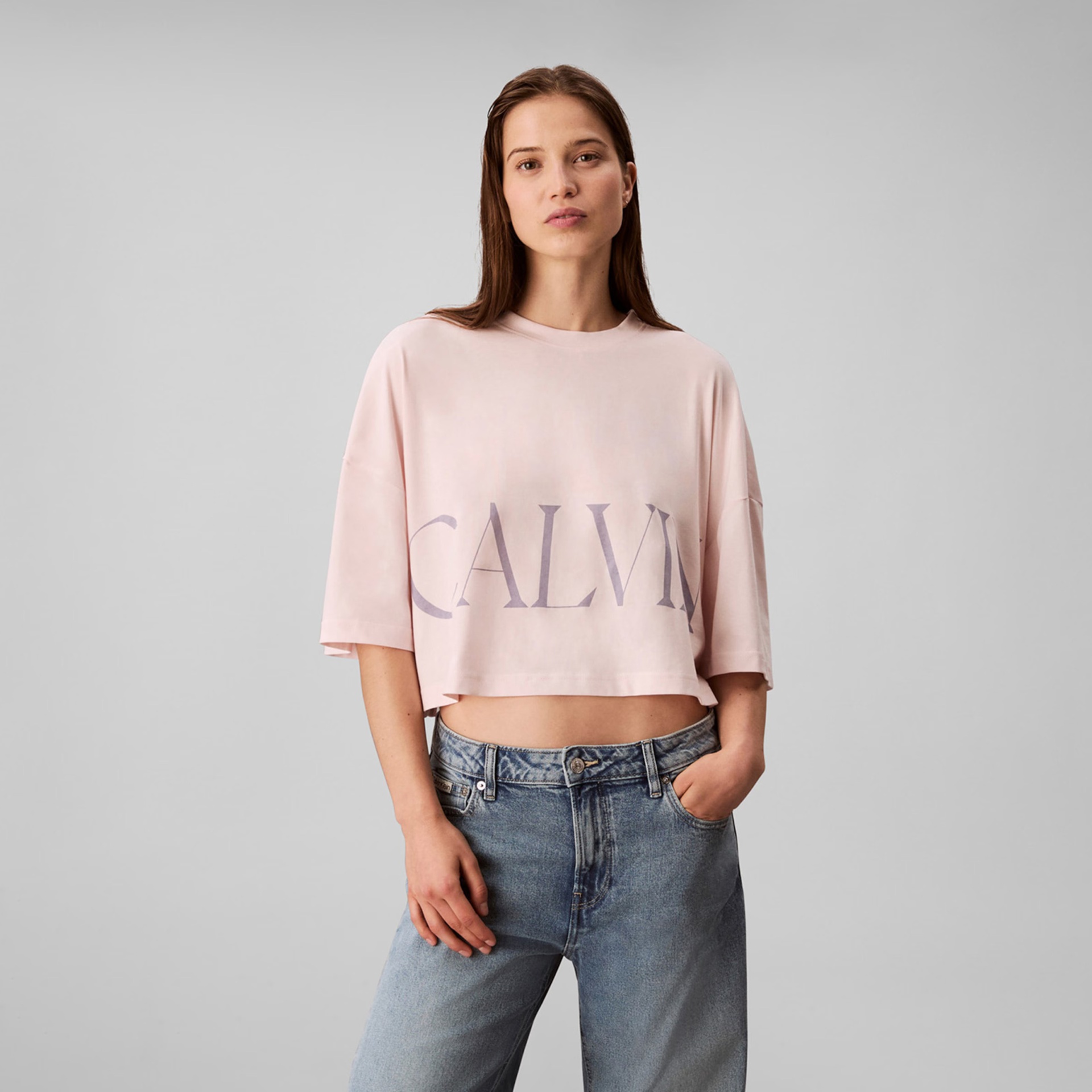 Camisola crop rosa claro com logótipo CALVIN e jeans azul clara.