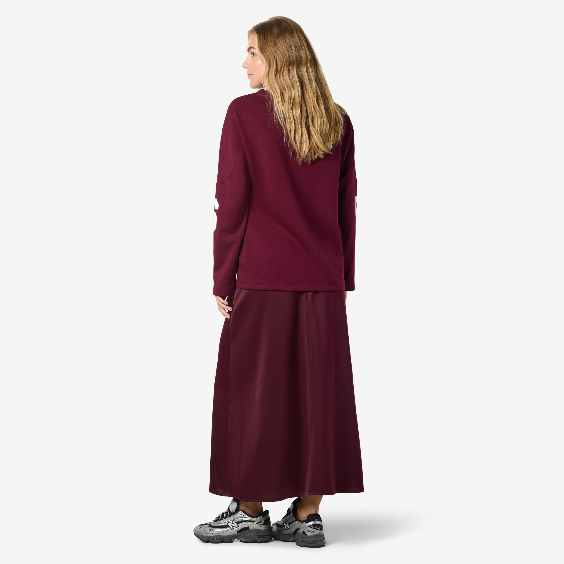 Mulher de costas com sweatshirt borgonha e saia longa borgonha, sapatilhas cinzentas.