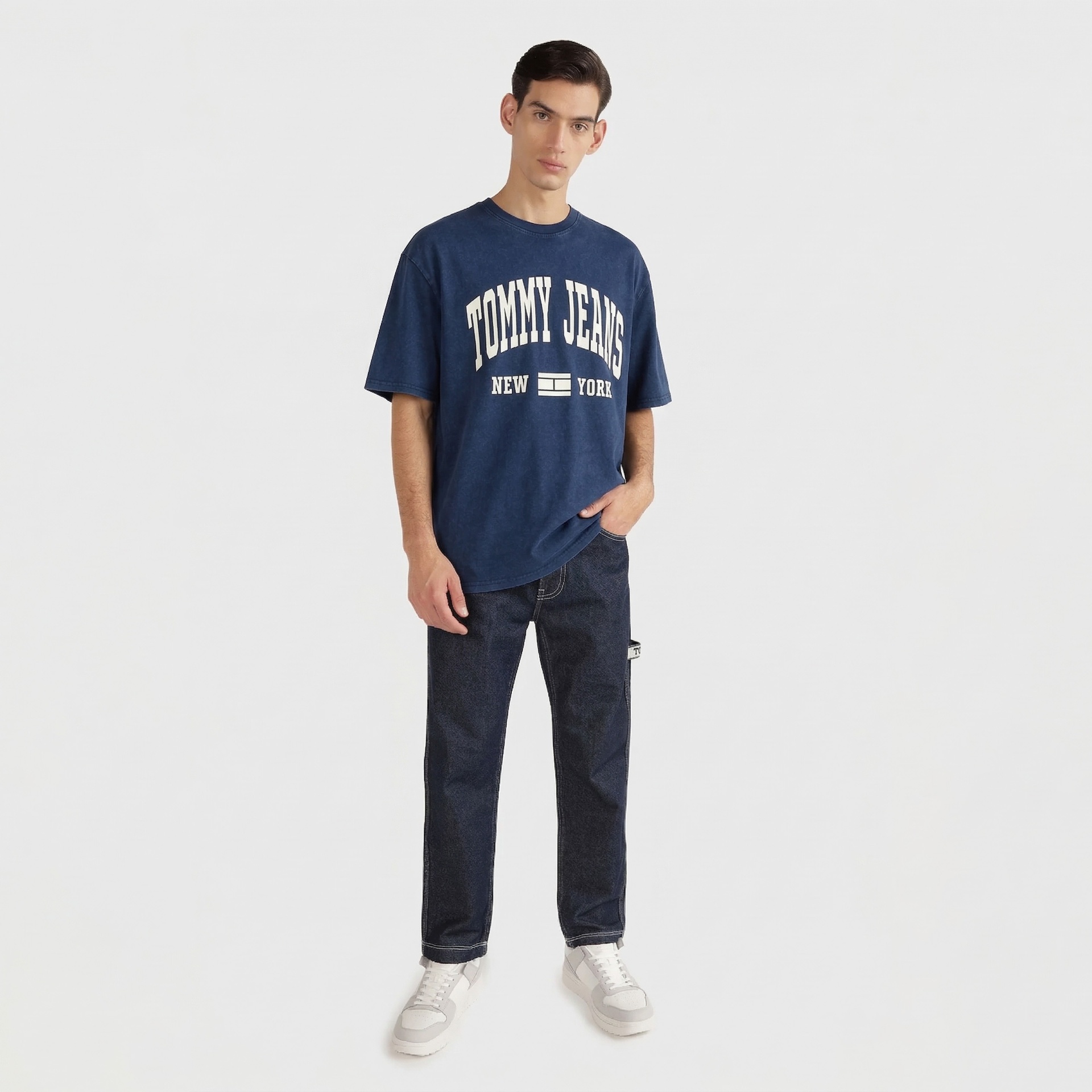 Homem vestido com camisola azul TOMMY JEANS e calças de ganga azuis com ténis brancos