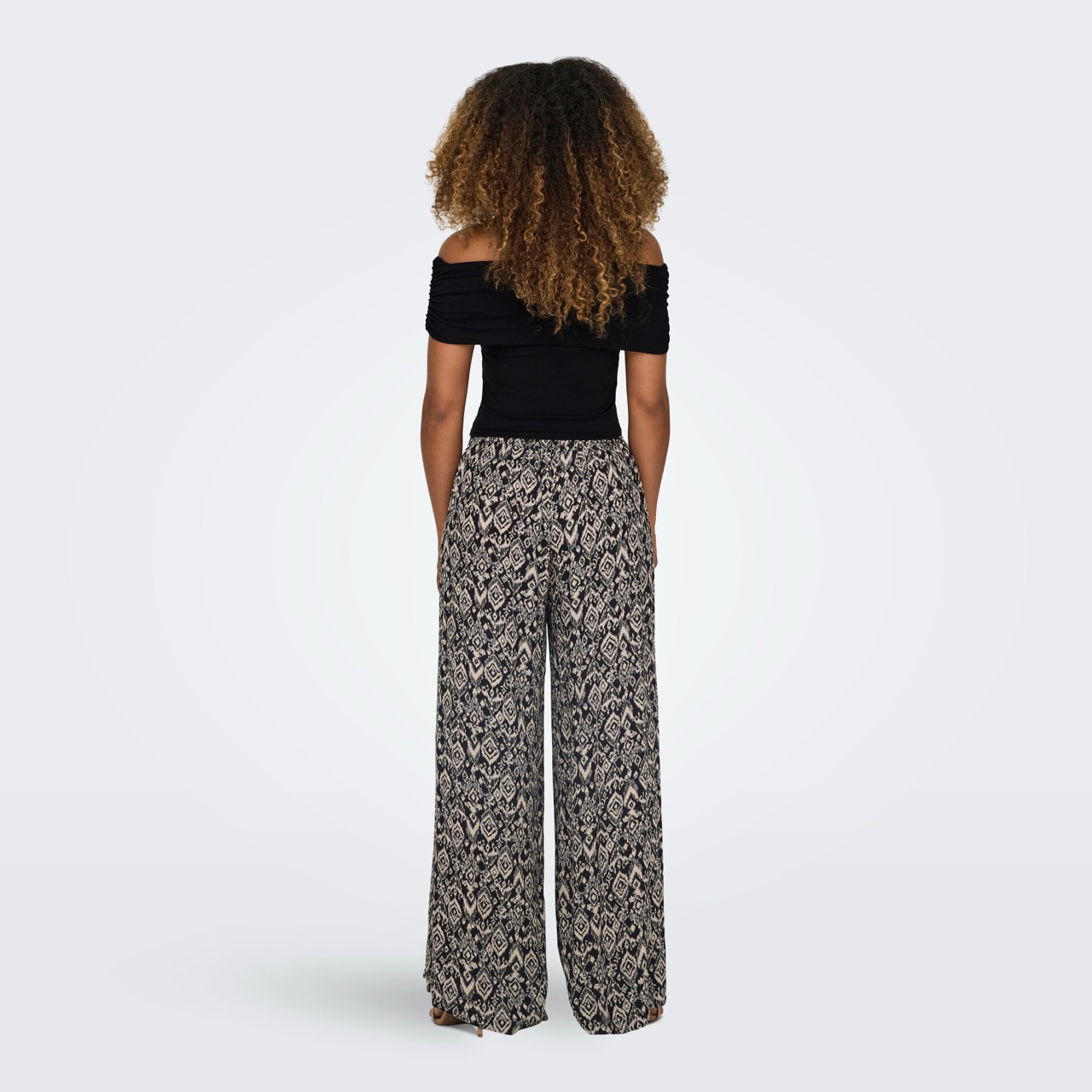 Mulher vista de costas a usar calças largas estampadas e top preto curto