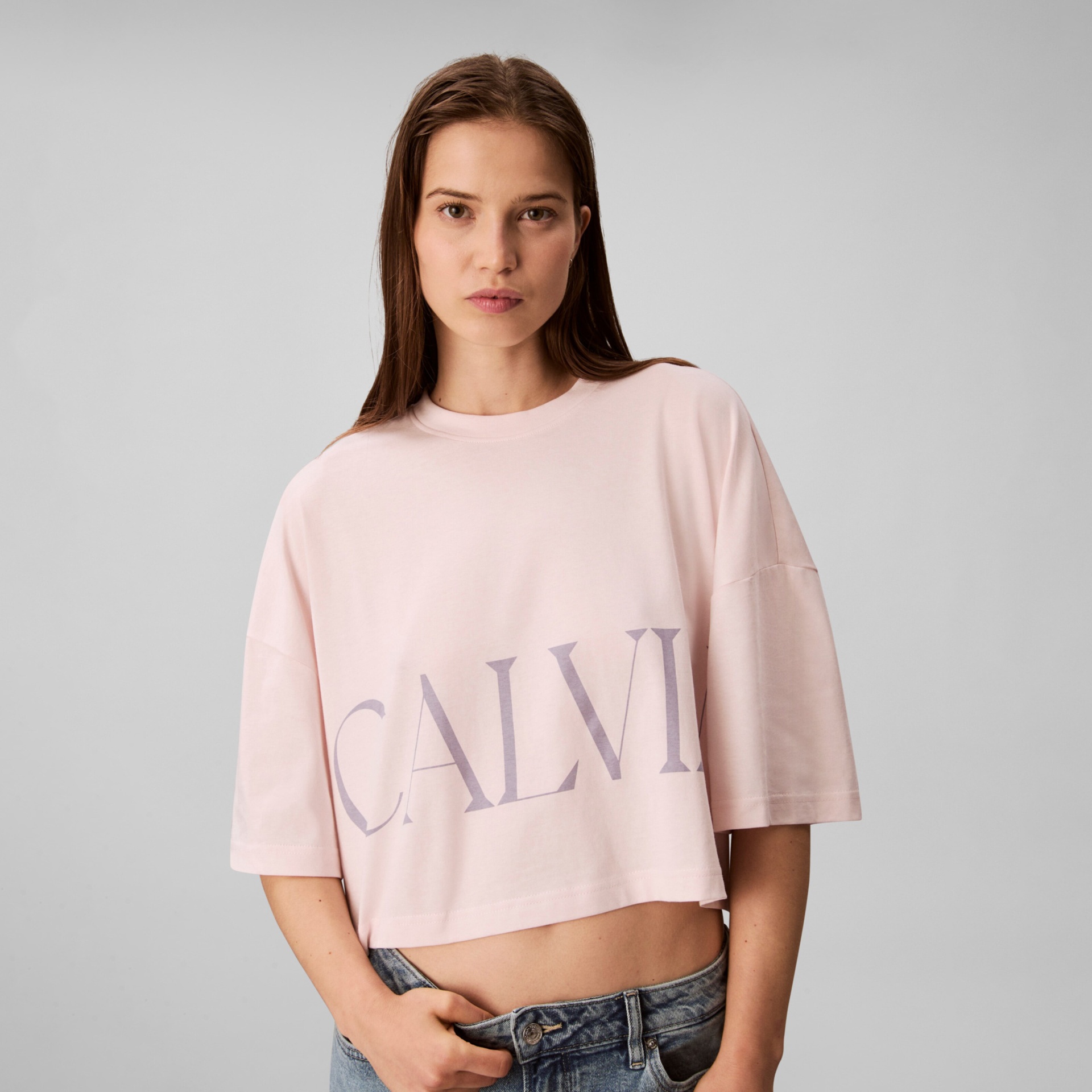 T-shirt cropped rosa claro com letras CALVI cinzentas e calças de ganga azuis