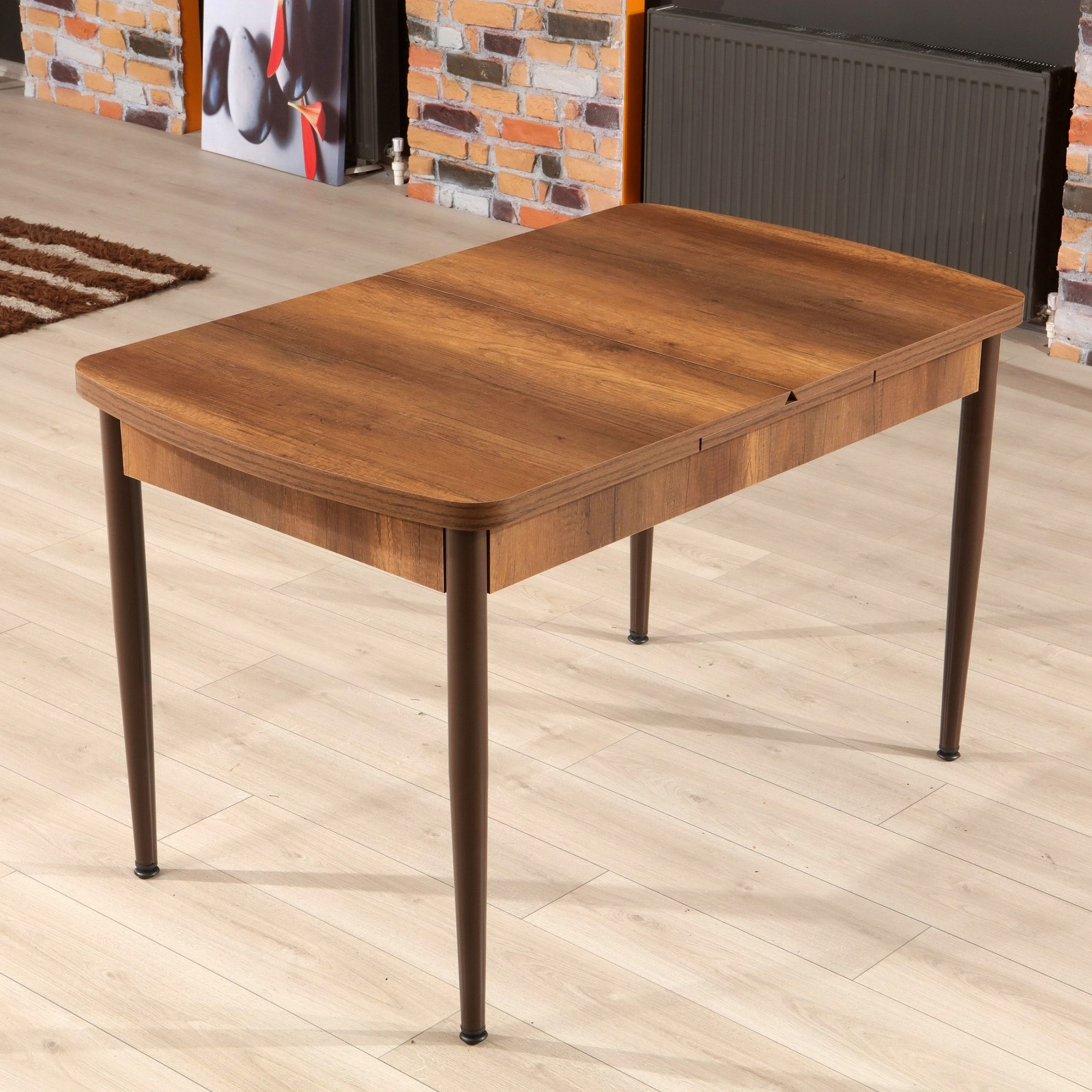 Mesa de jantar retangular em madeira castanha com pernas metálicas castanhas em ambiente interior com parede de tijolos.