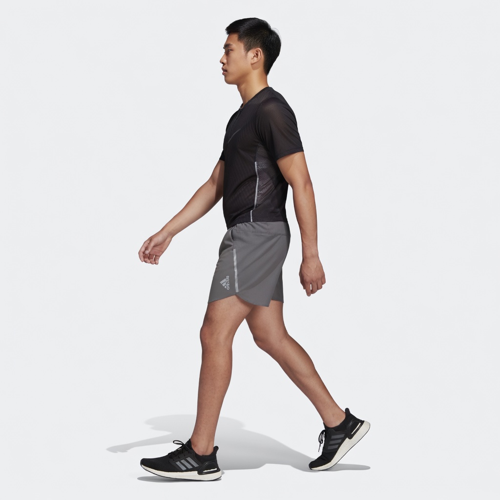 Homem com camisola preta, calções cinza e sapatilhas pretas Adidas em fundo branco.