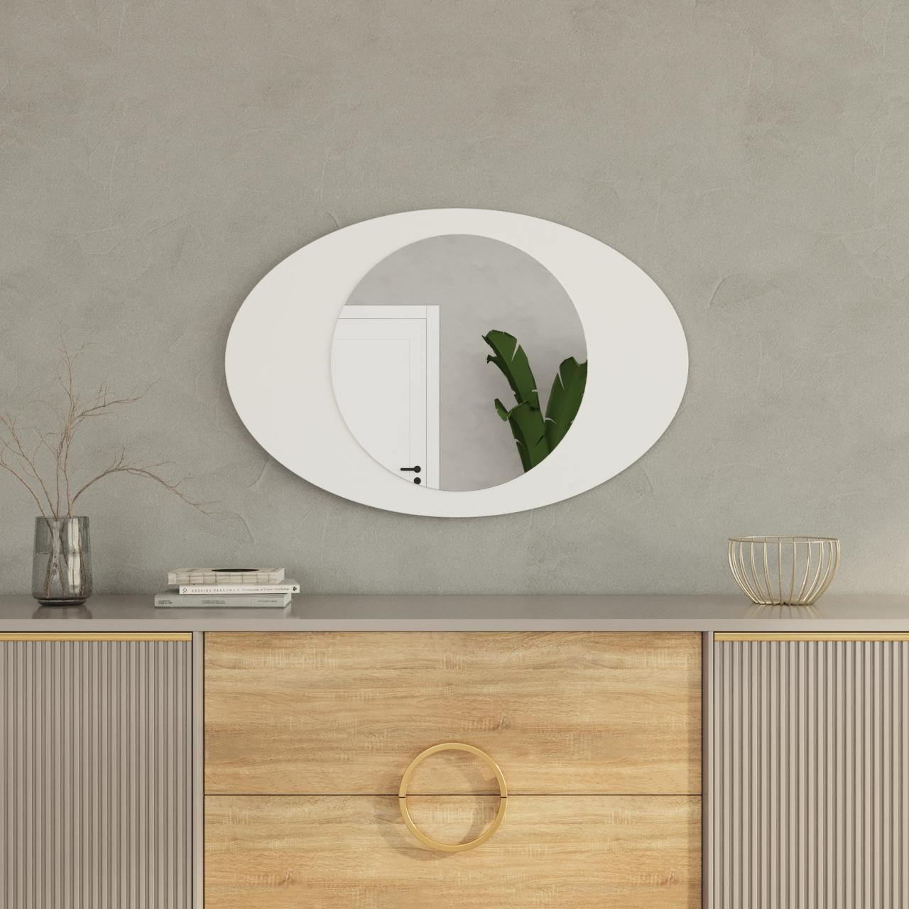 Espelho oval branco acima de móvel com madeira clara e cinza, decorado com vaso, livros e cesta dourada