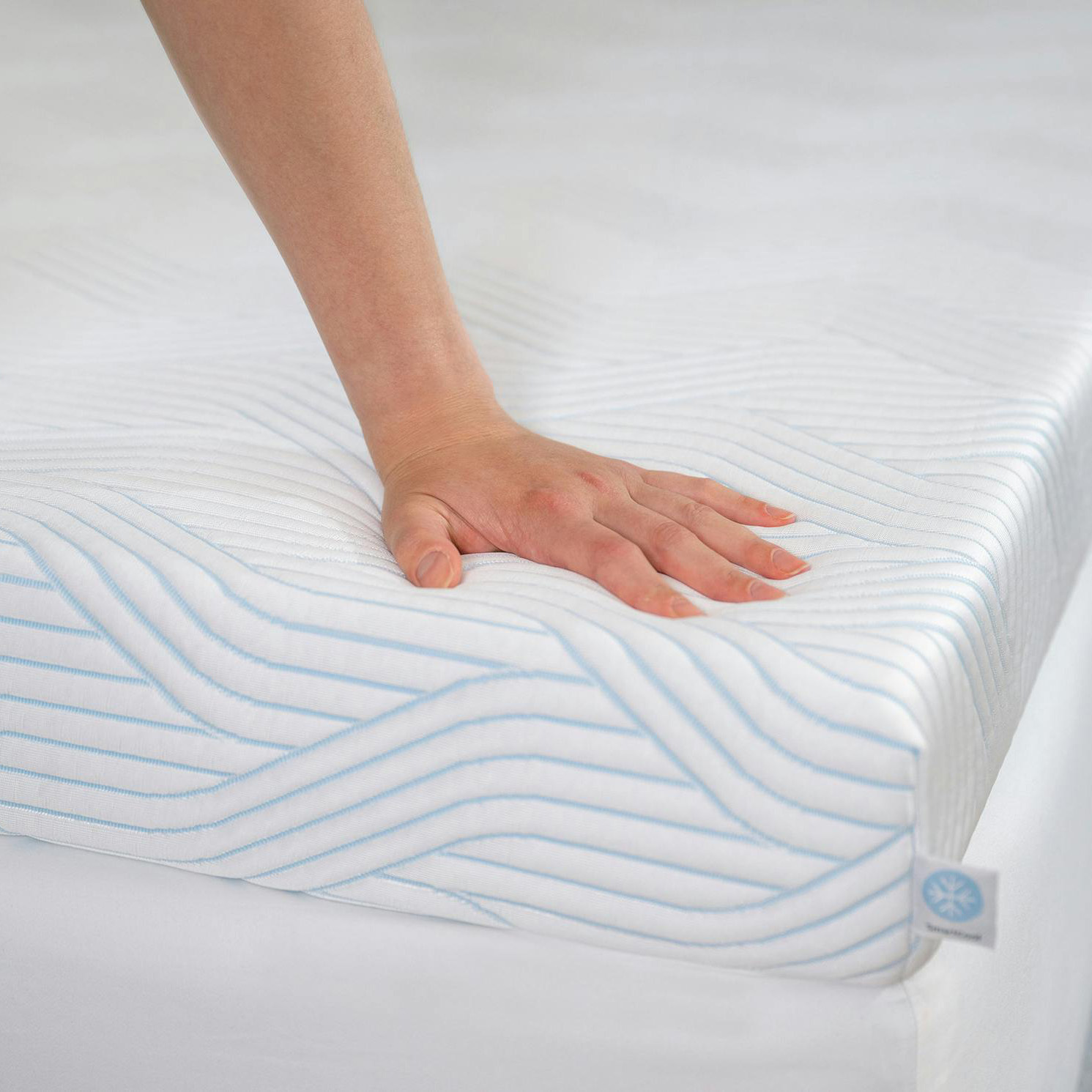 Colchão branco com linhas azuis e mão a pressioná-lo