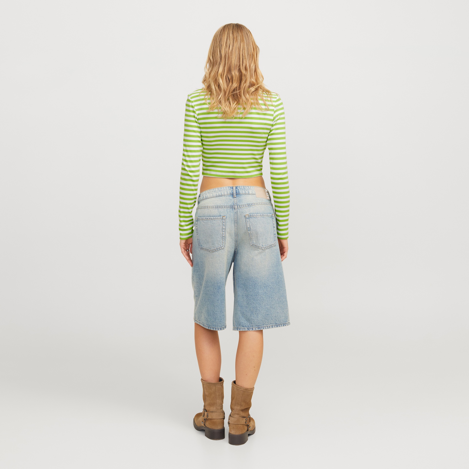 Pessoa de costas com camisola de riscas verde e branca, calções de ganga azul clara e botins castanhos.