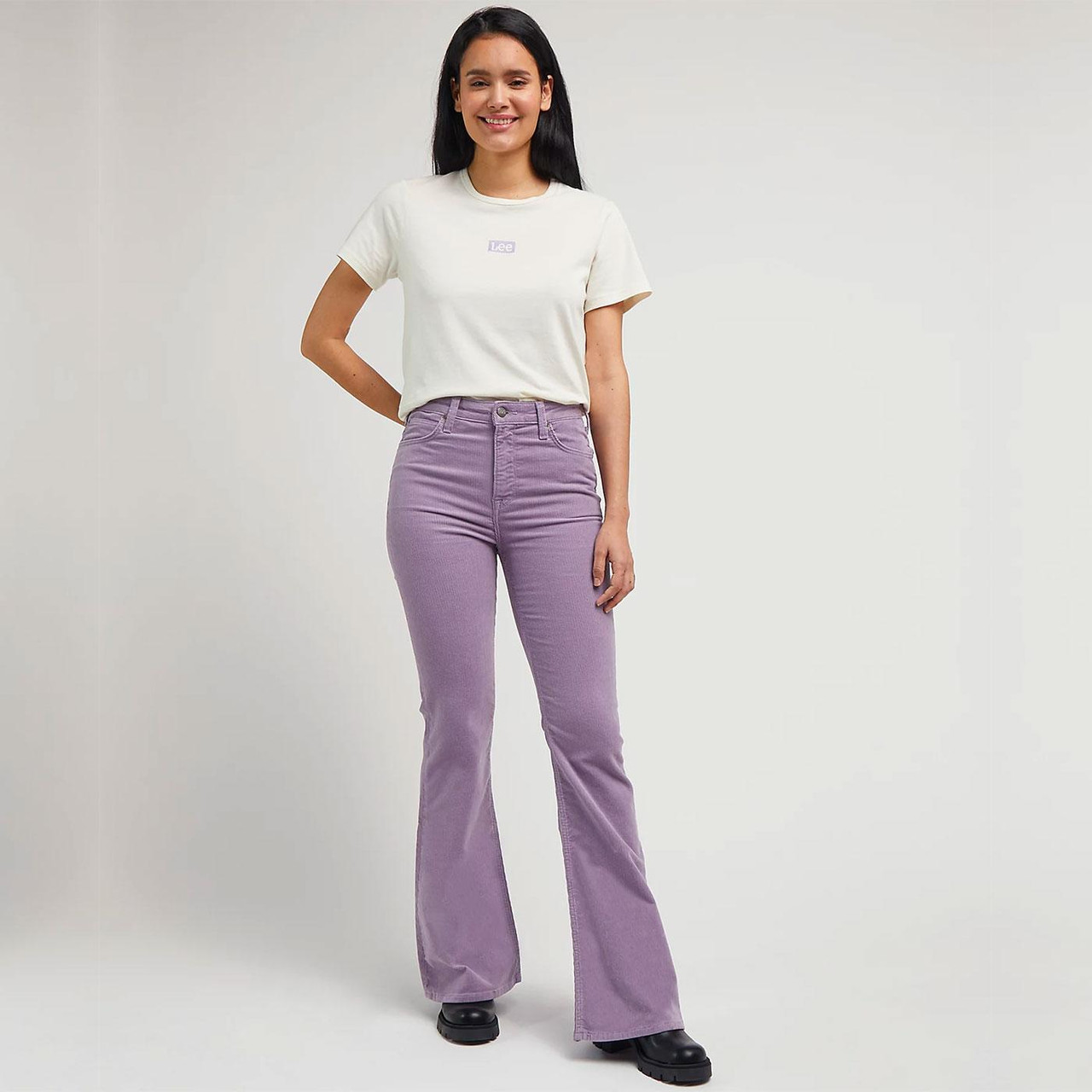 Mulher com t-shirt branca Lee, calças cor-de-rosa flare e sapatos pretos em fundo branco