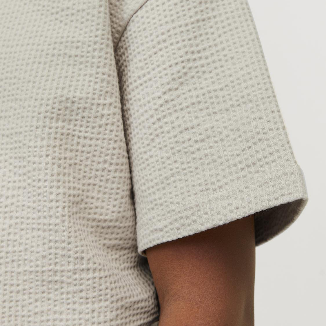 Manga curta de t-shirt bege com textura quadriculada em relevo num braço