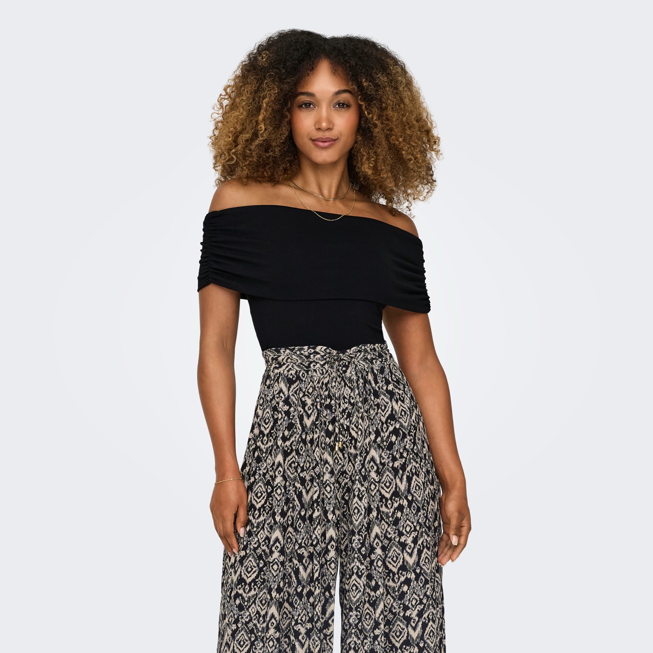 Mulher de blusa preta ombro a ombro e calças largas com padrão geométrico