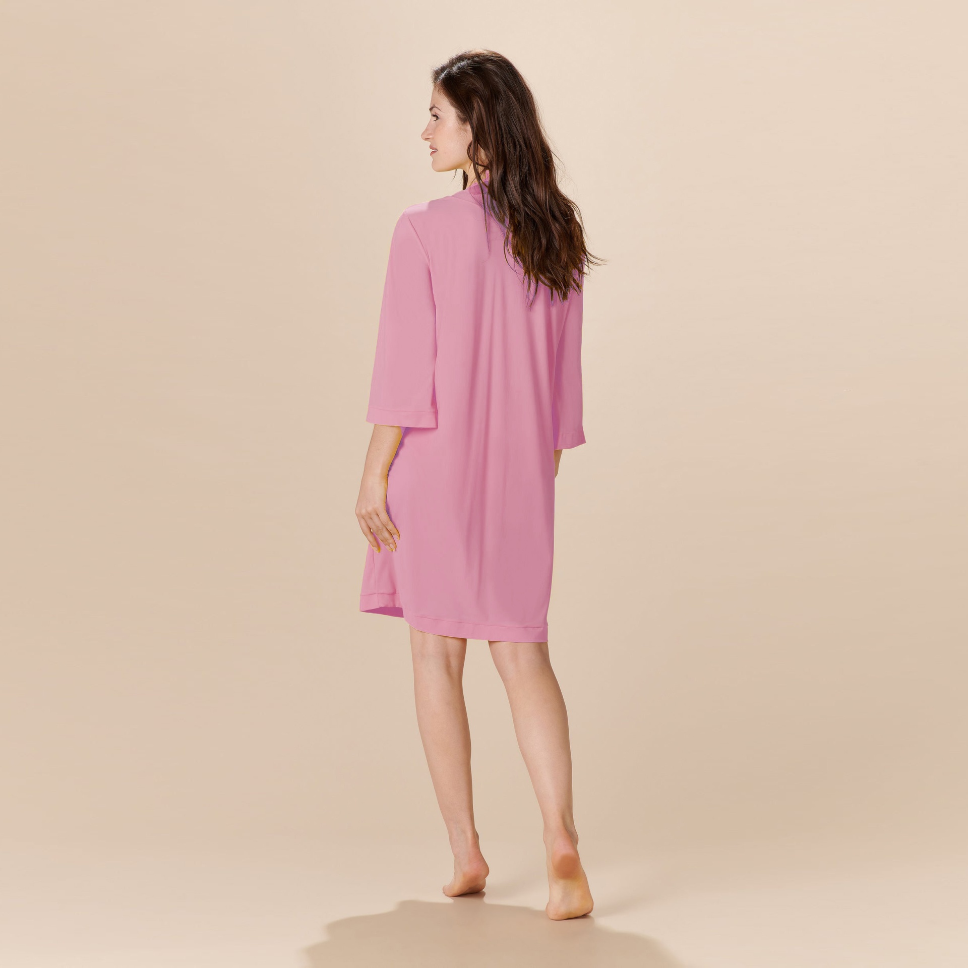 Vestido rosa curto de costas com mangas três quartos e gola alta.