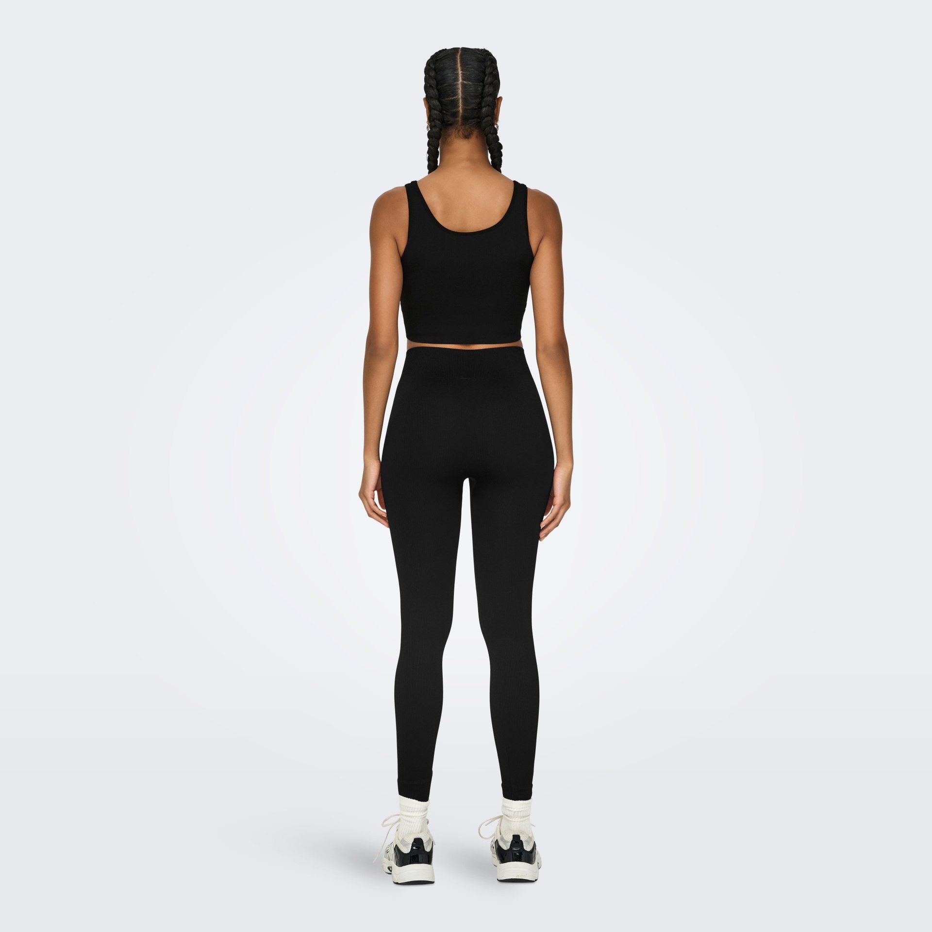 Mulher vestindo top cropped e leggings pretas, vista de costas, com ténis brancos e meias brancas.