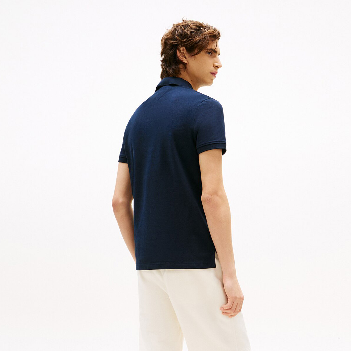 Homem de costas com polo azul-marinho e calças brancas