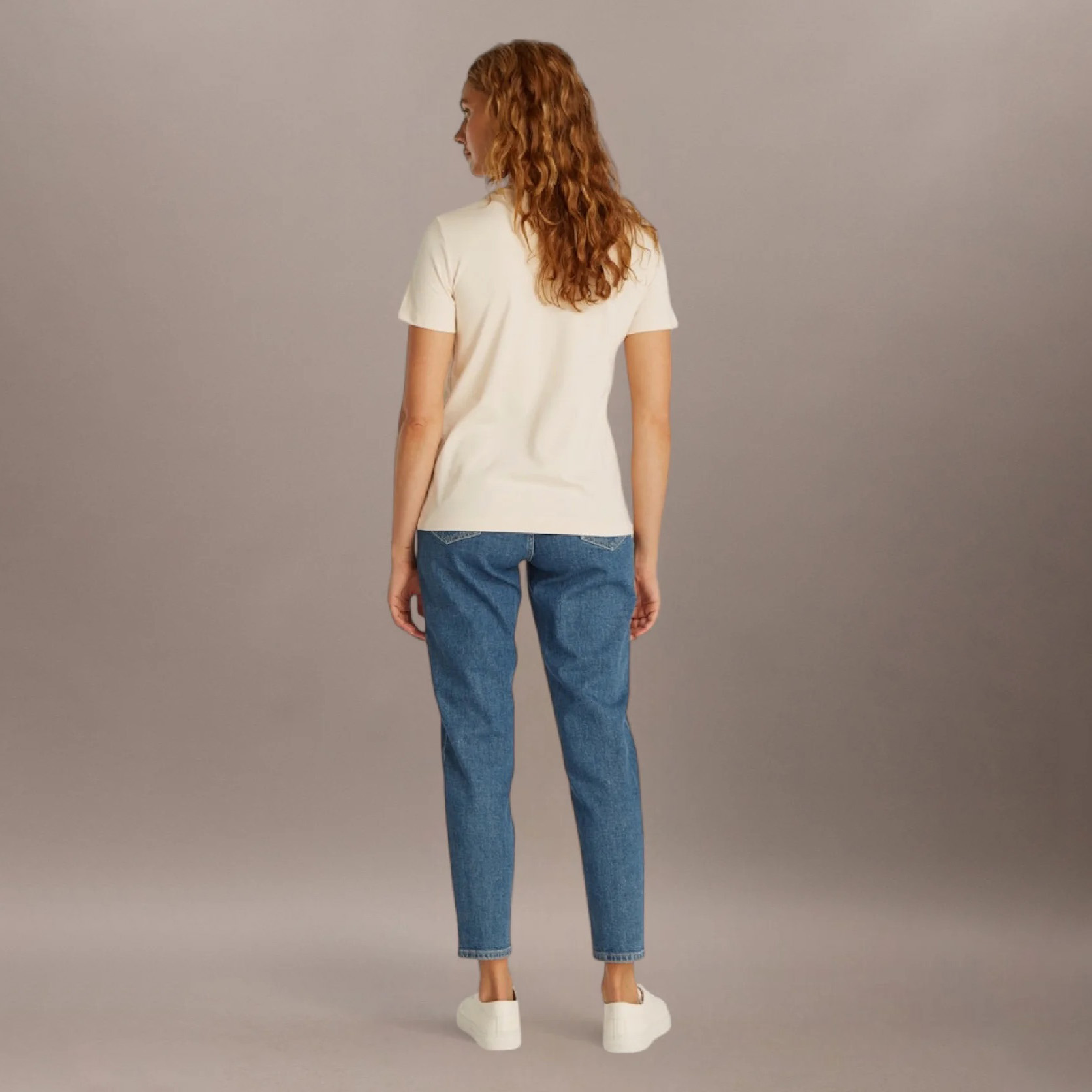 Mulher com camisola creme, jeans azuis e sapatilhas brancas vista de costas