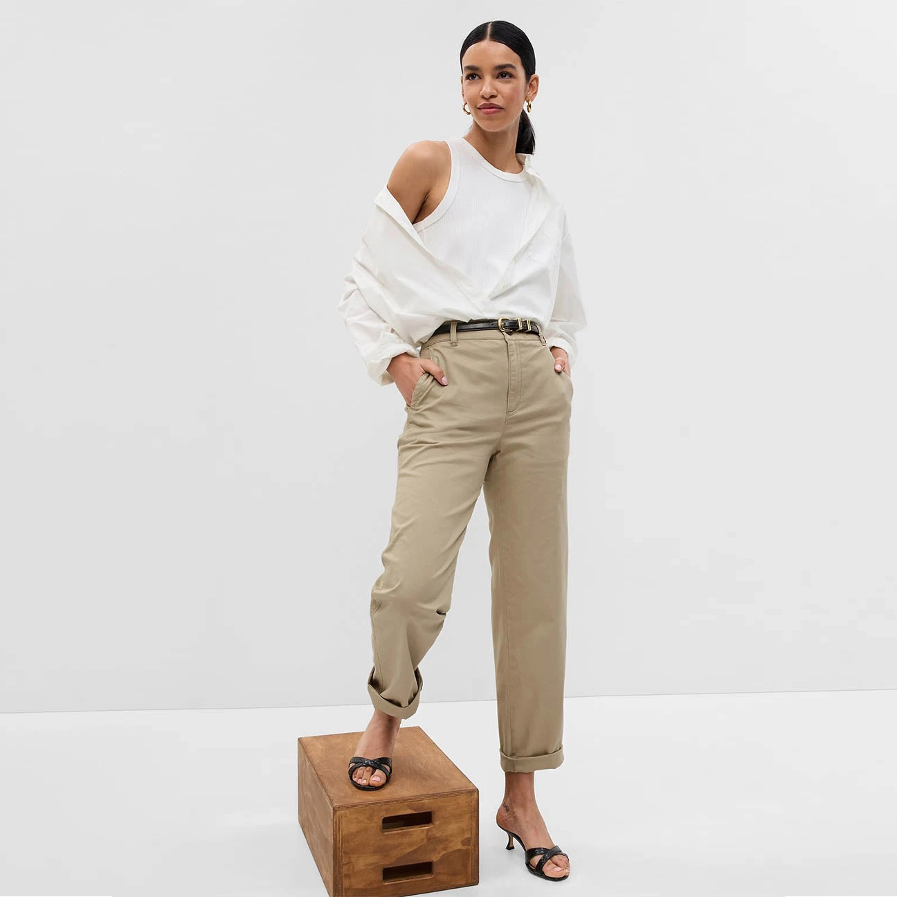 Pessoa com roupa casual branca e bege, calçando sandálias pretas, sobre fundo branco