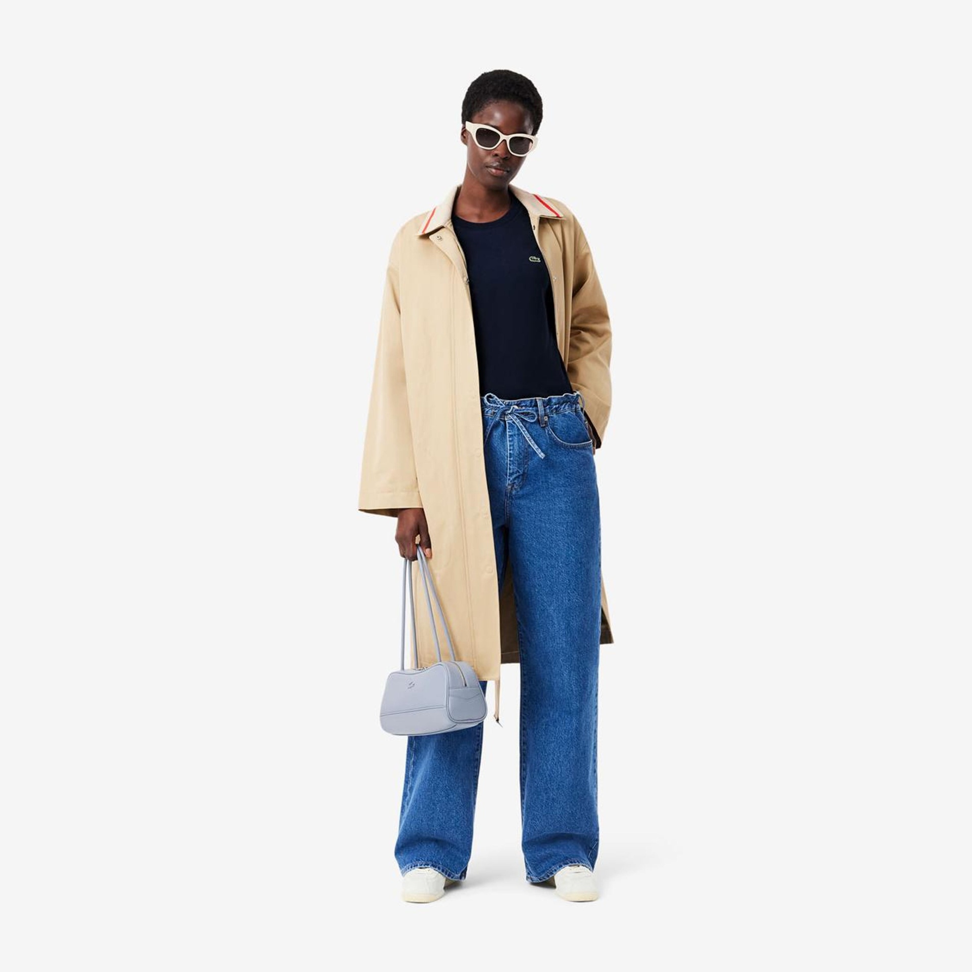 Homem com casaco bege, jeans azuis largos e bolsa cinza