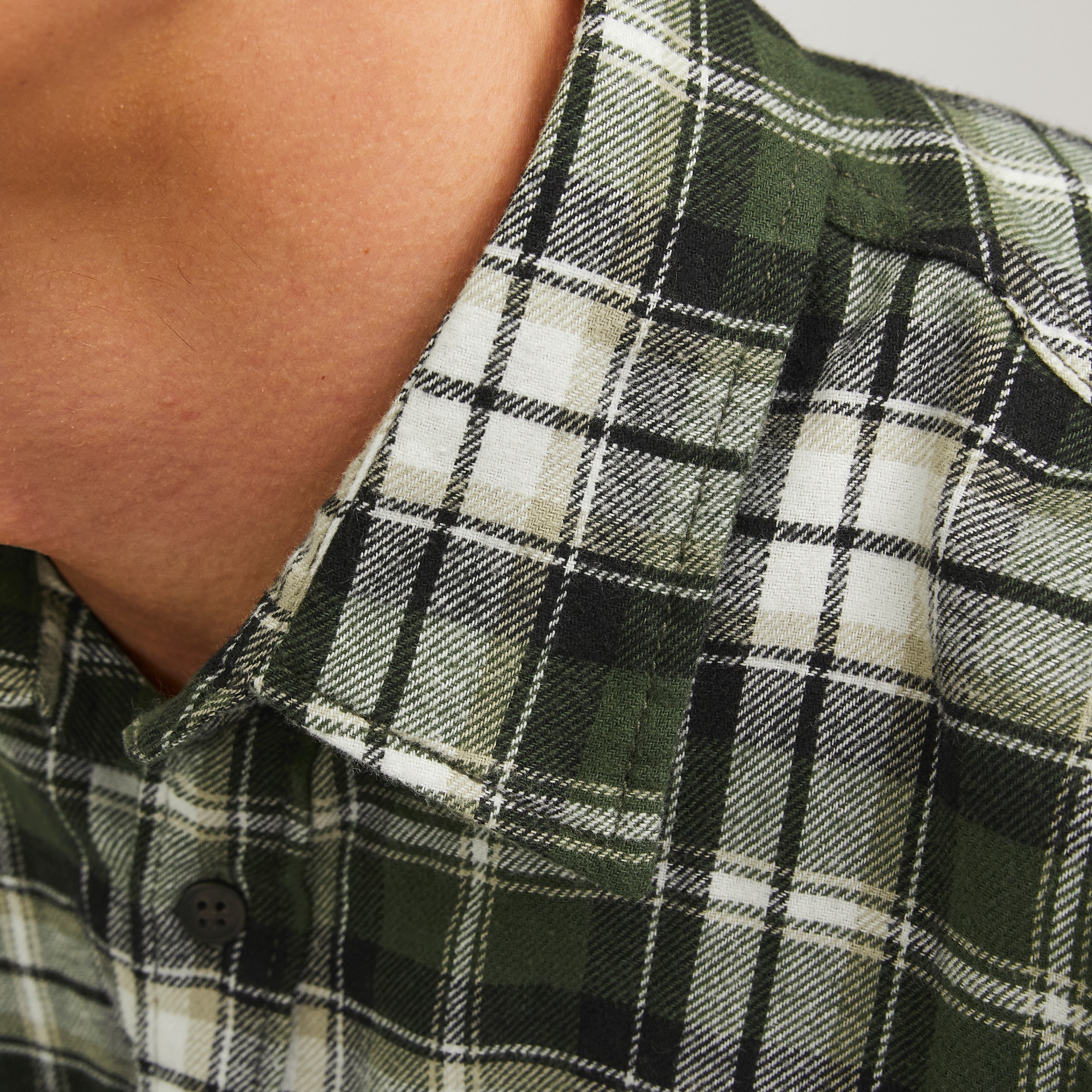 Camisa xadrez verde e branco de flanela com botão preto no colarinho.