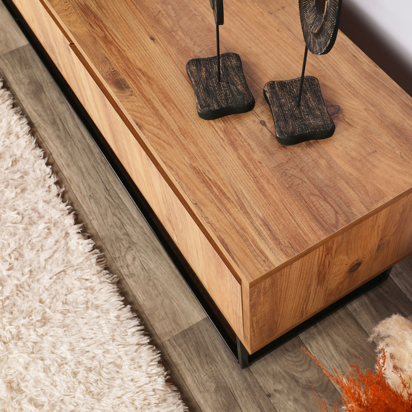 Móvel de madeira clara com esculturas em madeira escura, chão de madeira cinzenta e tapete branco peludo