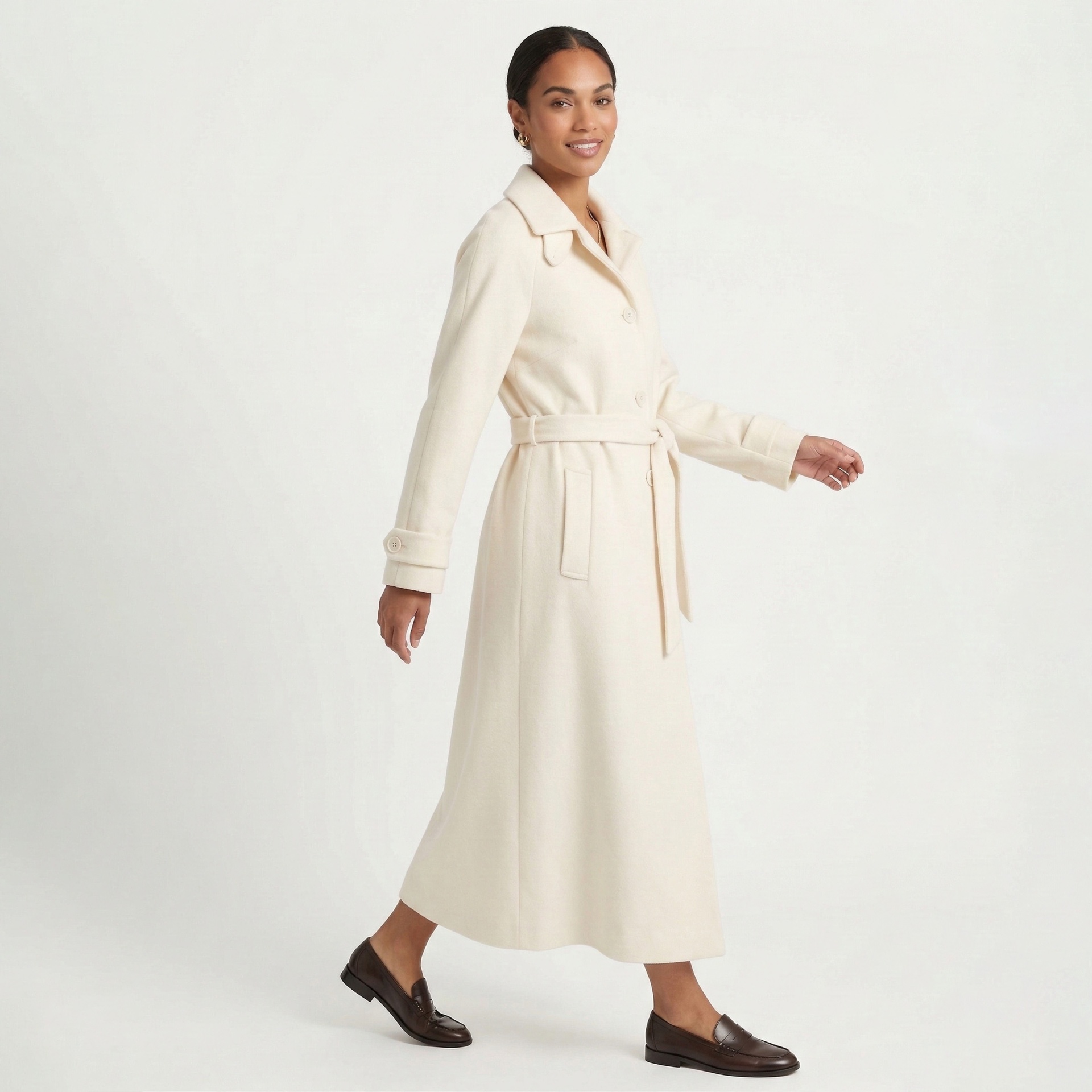 Casaco comprido creme com cinto e botões usado por mulher em fundo branco
