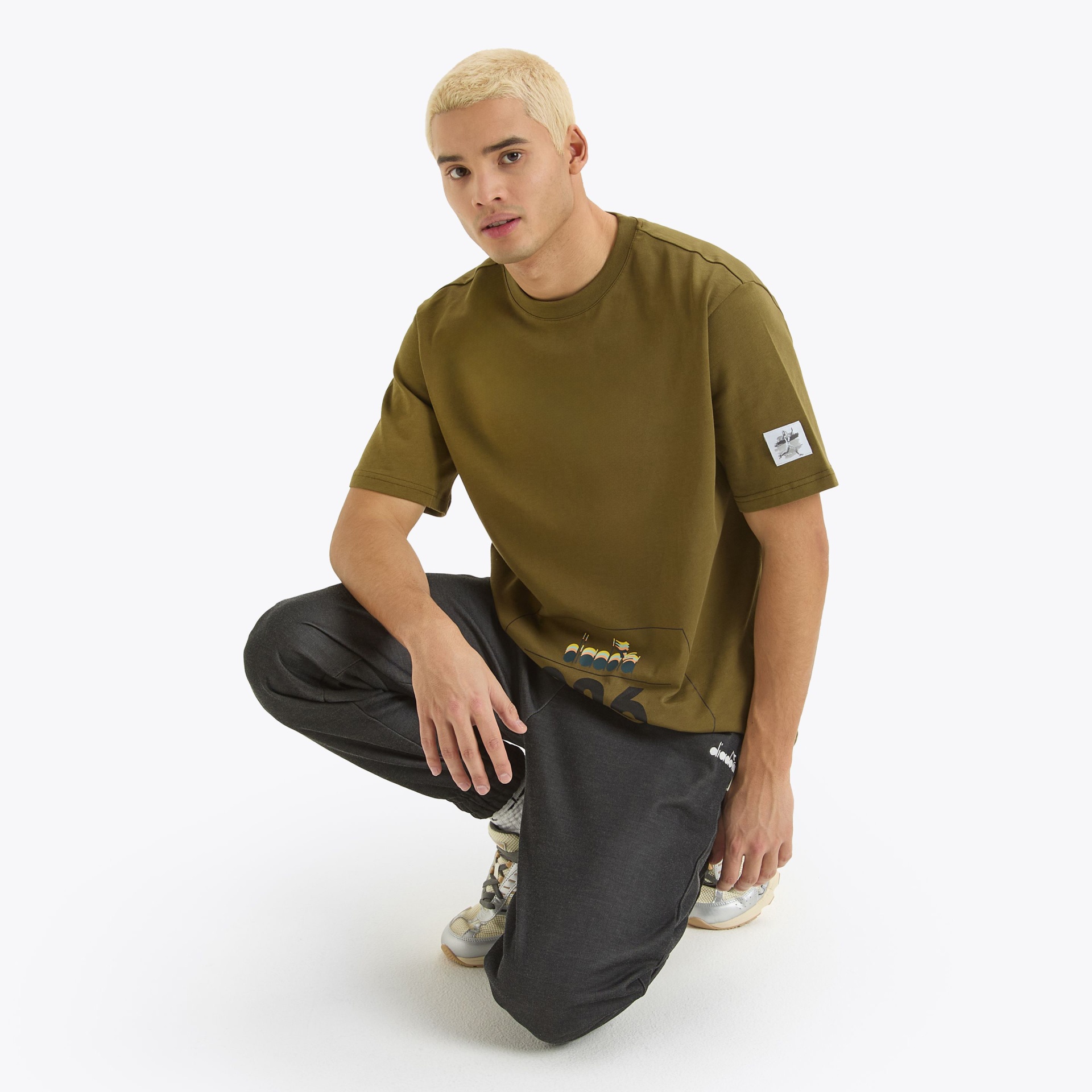 T-shirt verde-oliva e calças pretas em modelo ajoelhado