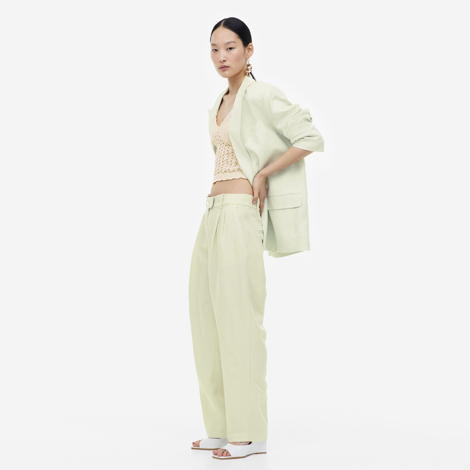Mulher com blazer e calças bege claro, blusa crochet creme e sandálias brancas