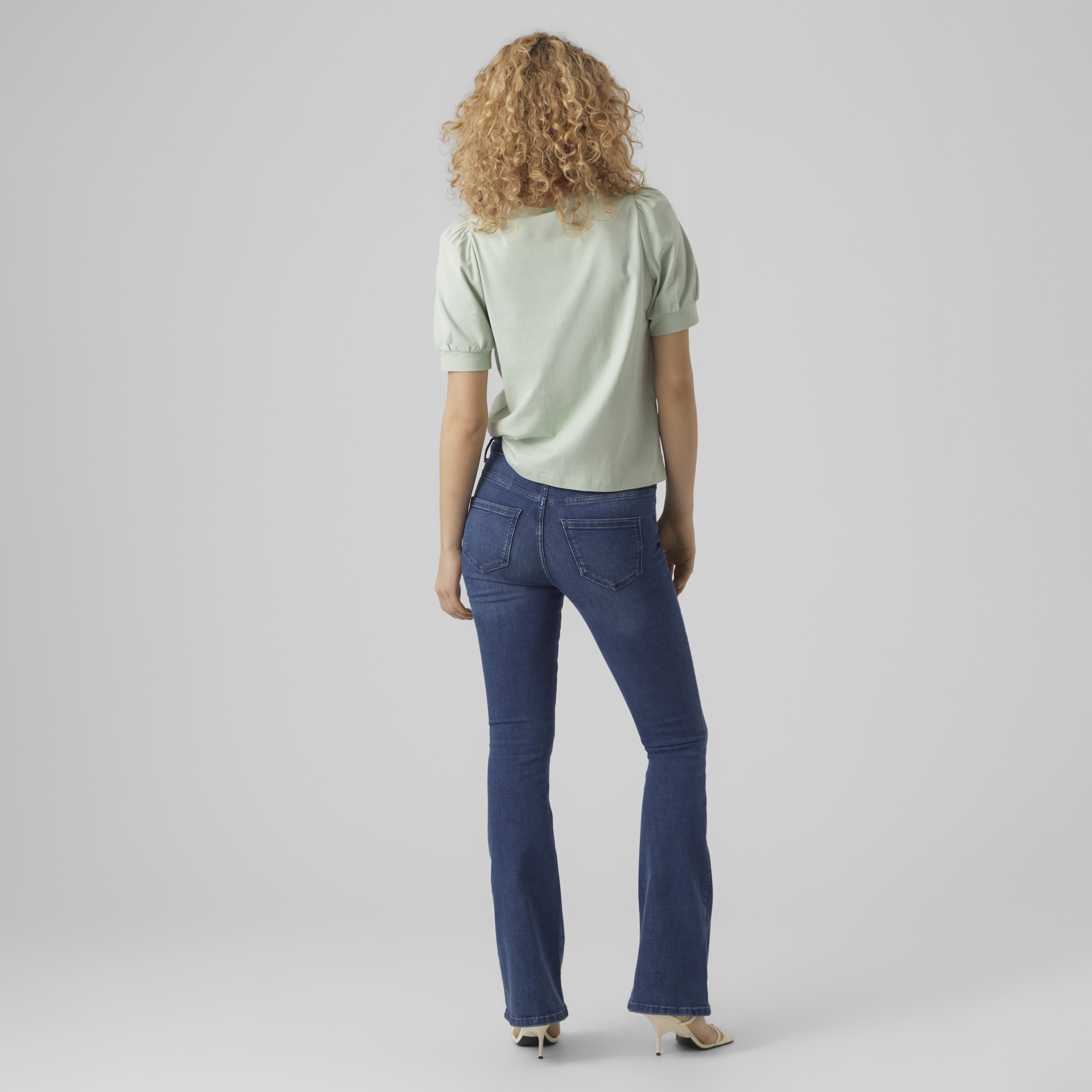 Mulher de costas com calças de ganga, blusa verde clara e sapatos bege.