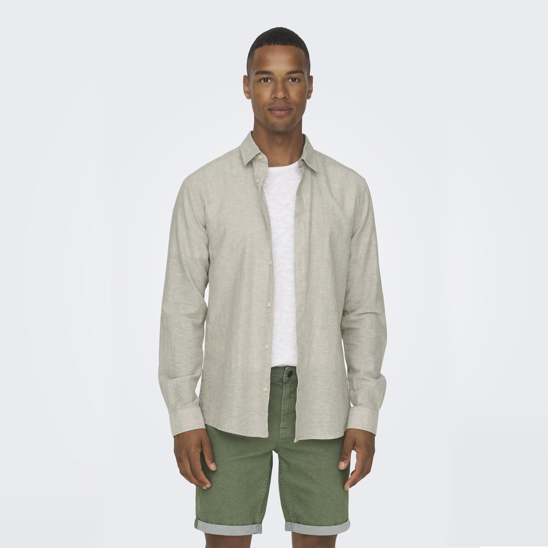 Homem com camisa bege, t-shirt branca e calções verdes em fundo branco