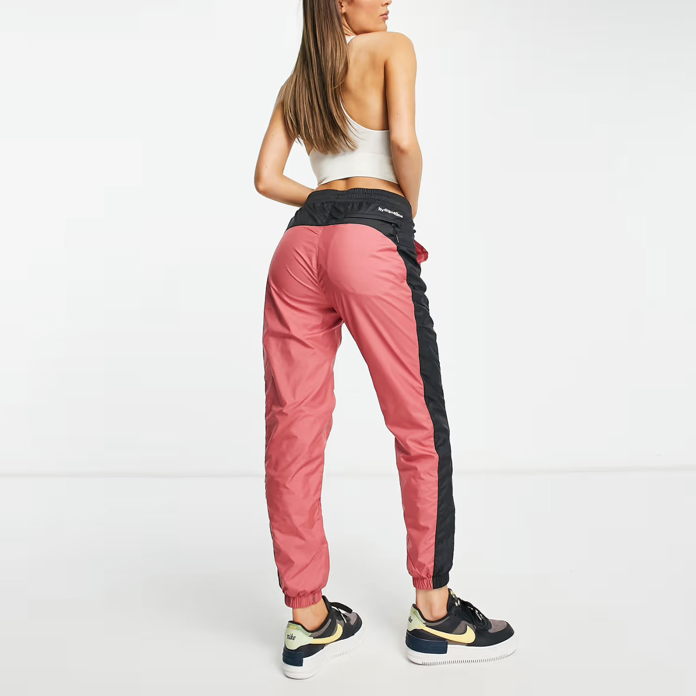 Calças desportivas rosa com risca preta e cós elástico preto, calçadas com ténis Nike em fundo branco