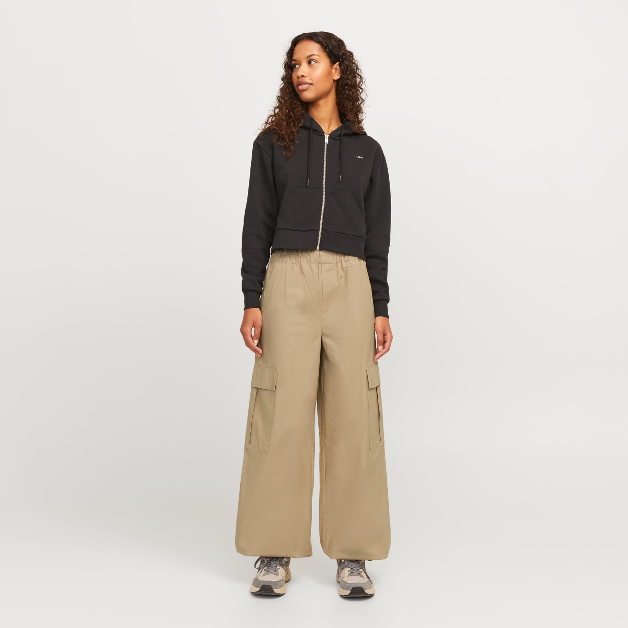 Mulher a usar casaco preto com capuz e calças largas cargo bege