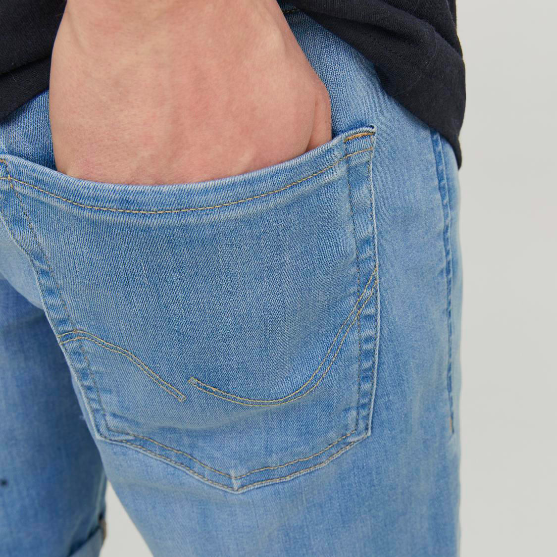 Mão num bolso traseiro de calças de ganga azuis claras com costuras visíveis.