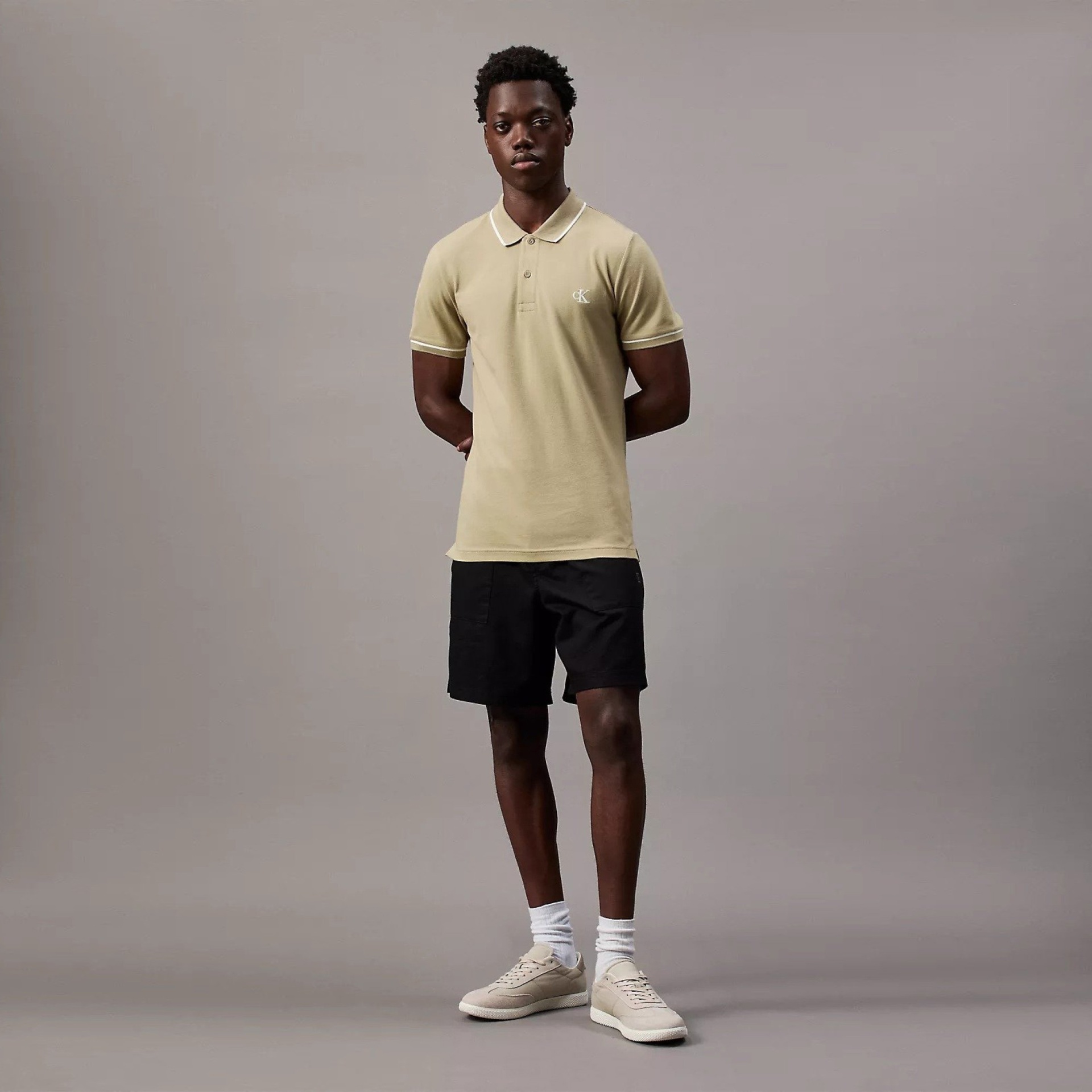 Homem vestido com polo bege, calções pretos, meias brancas e sapatilhas bege