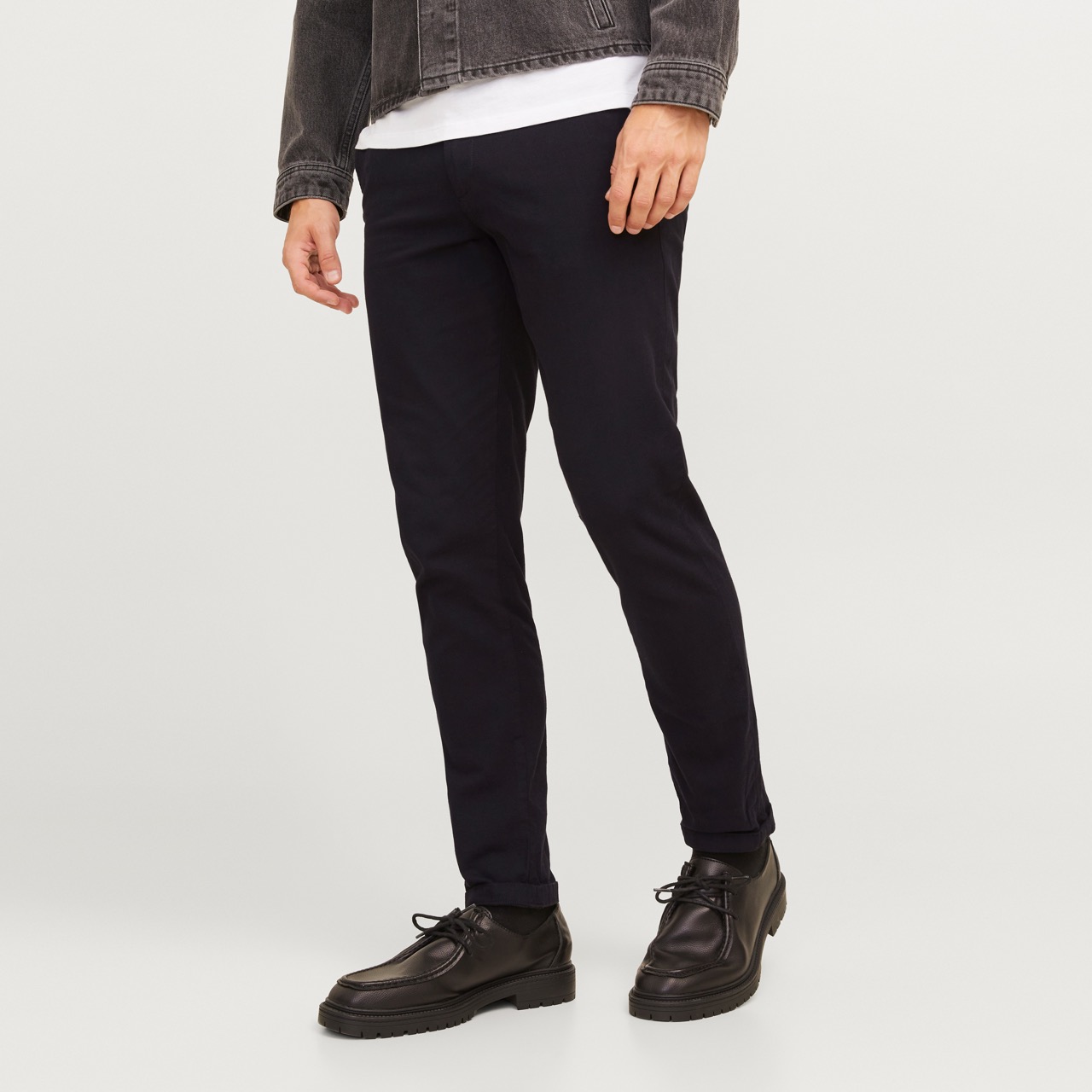 Calças azuis-escuro de corte justo usadas por homem com sapatos pretos sobre fundo branco